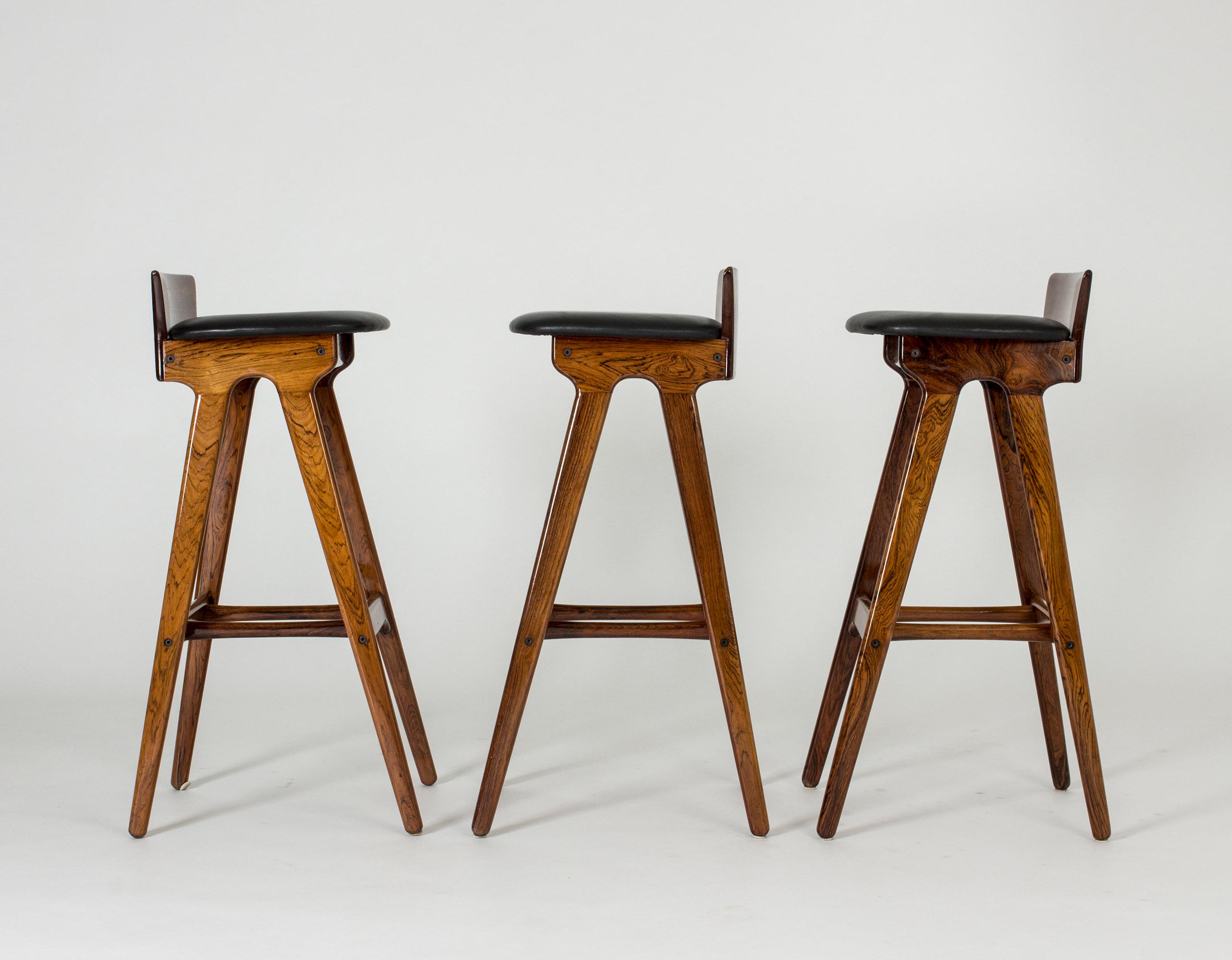 Set of three cool bar stools by Erik Buch, made from rosewood and black leather. Beautiful sheen in the wood, cool silhouettes.