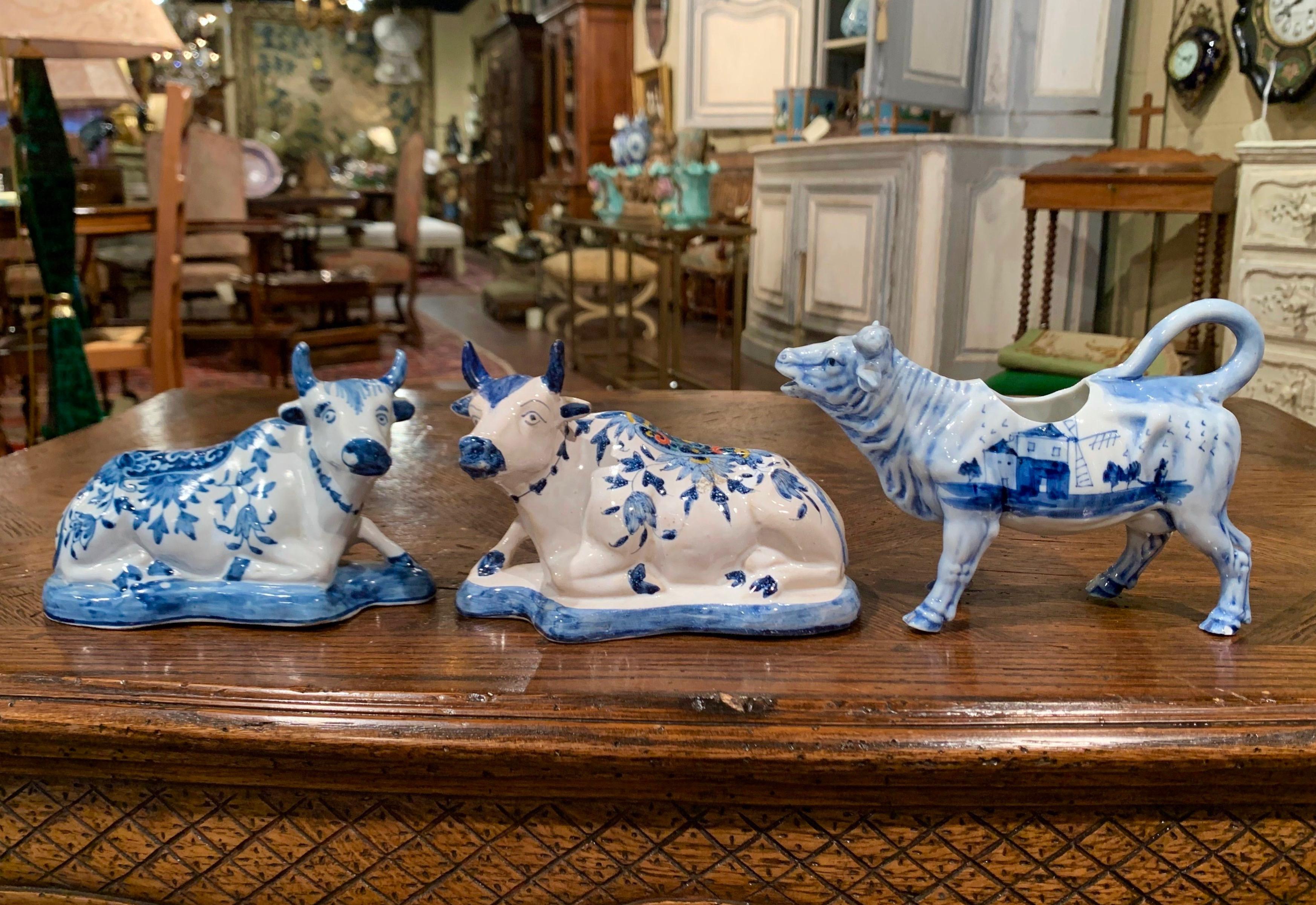 Crafted in Holland circa 1960, the three porcelain cow sculptures are hand painted in the traditional Delft blue and white colors with floral and sailboat motifs. Each bovine figure is stamped on the bottom with initials. The three pieces are in