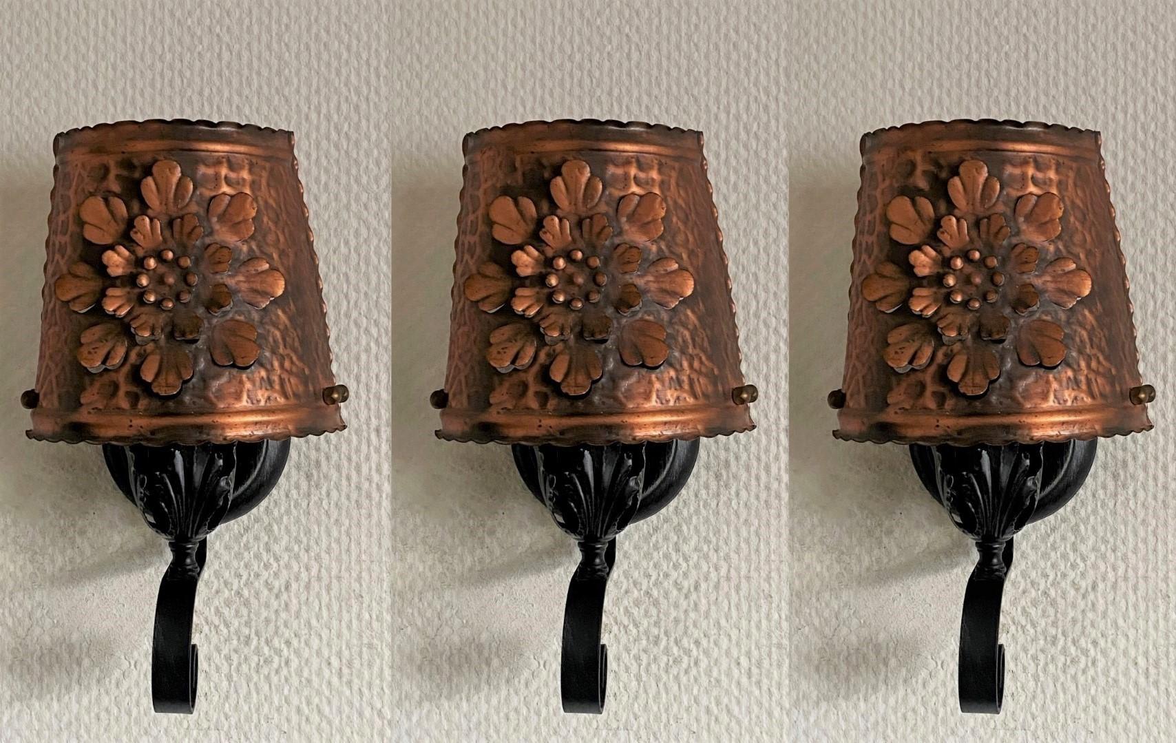 A set of three craftsman style wrought iron wall sconces with hand-hammered copper detailing, pierced details on the shades for light projection, Spain, 1950s. All 3 pieces in very good condition, with aged patina and rewired. Each sconce takes one