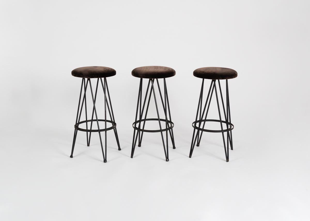 A set of three wrought iron bar stools with plush seats and remarkable geometric bases.