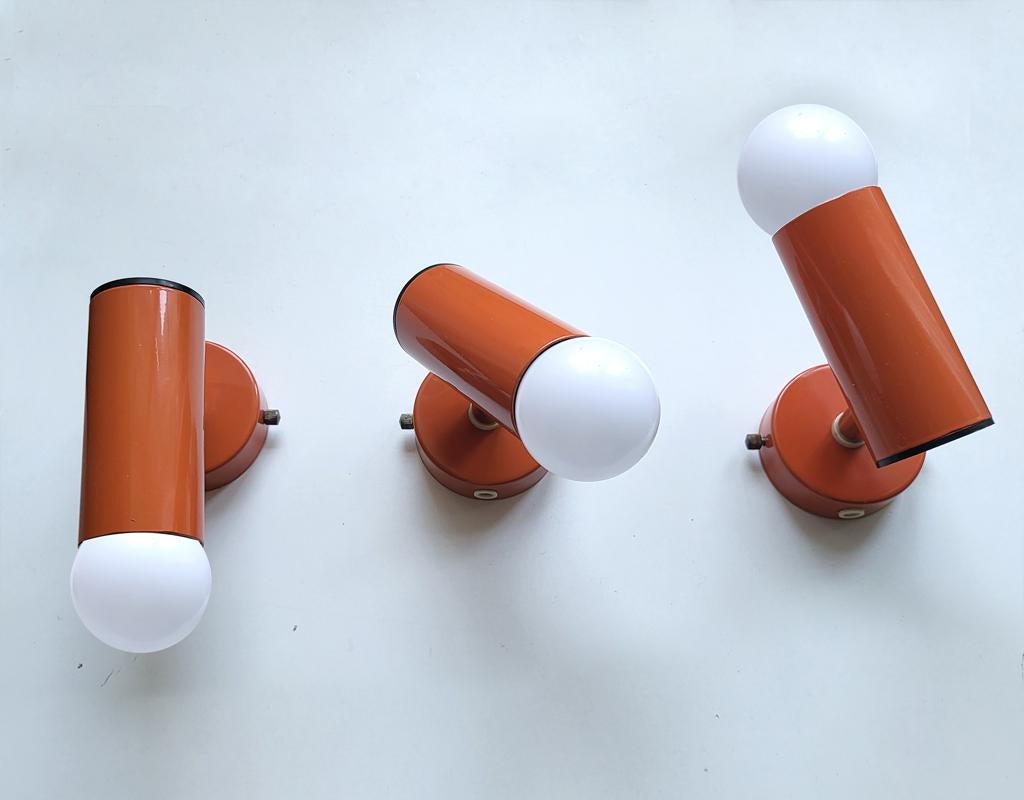 Set aus drei verstellbaren, orange lackierten Metall-Wand- (oder Decken-) Scheinwerfern mit bündiger Montage.
Deutschland, 1960er-1970er Jahre.
Lampenfassungen: E27 (für  US: E26)

 