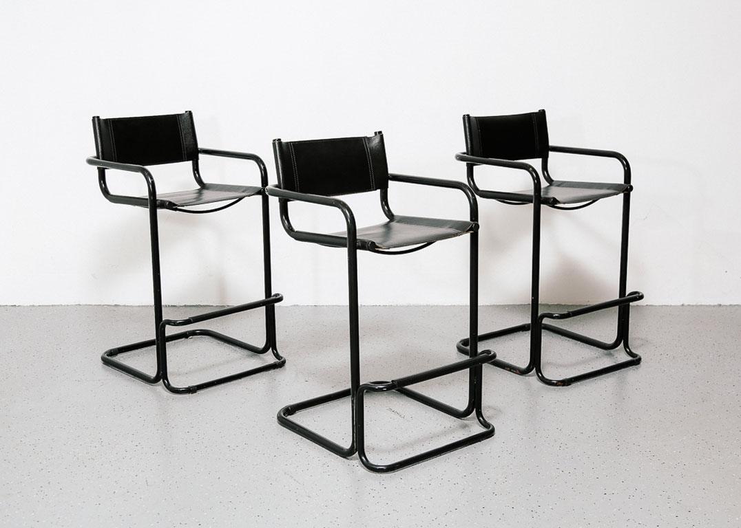Set of three bar stools with black cantilevered tubular frames, black leather sling seats, and foot rests. In the style of Bauhaus designer Mart Stam. 24.5