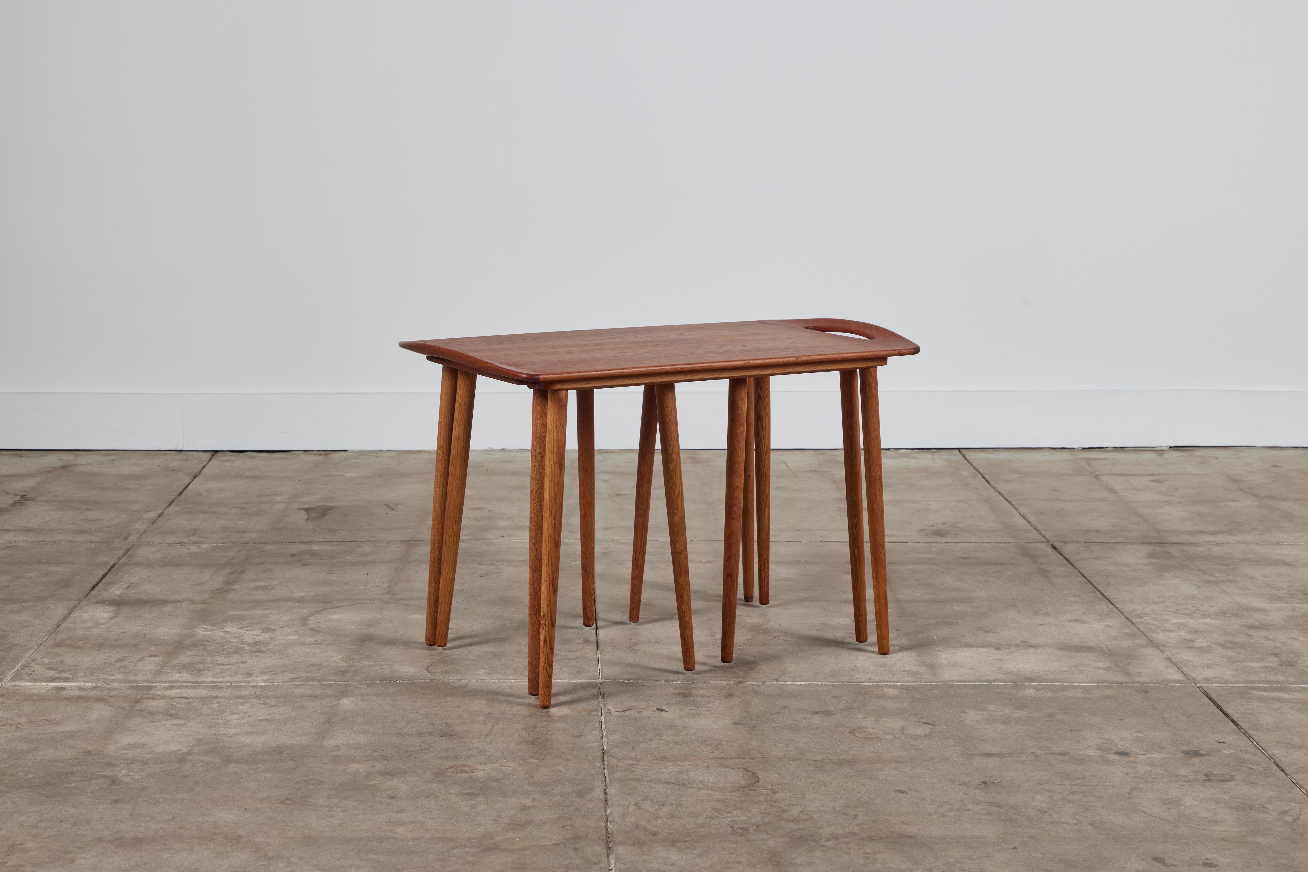 Set of nesting tables in teak for Mogens Kold, circa 1950s, Denmark. The set features a larger rectangular table with slightly curved edges with cutout handles. Two square nesting tables fit neatly under the larger table. All the tables have tapered