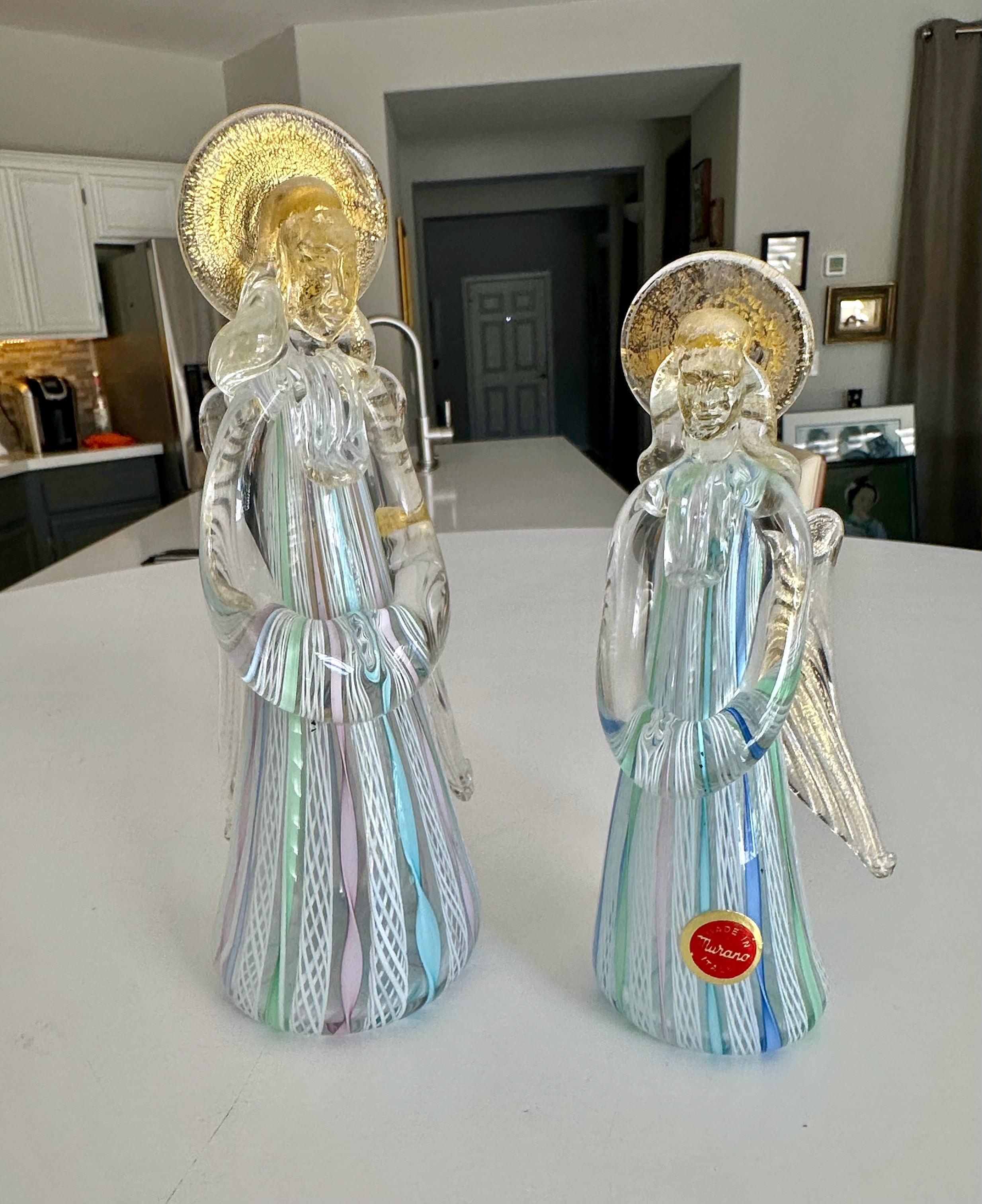 Coppia di statuette di Art Angels in vetro artistico di Murano, eseguite con filigrana latticino (motivo a canne) e dettagli in avventurina dorata. 
L'angelo più alto misura 8