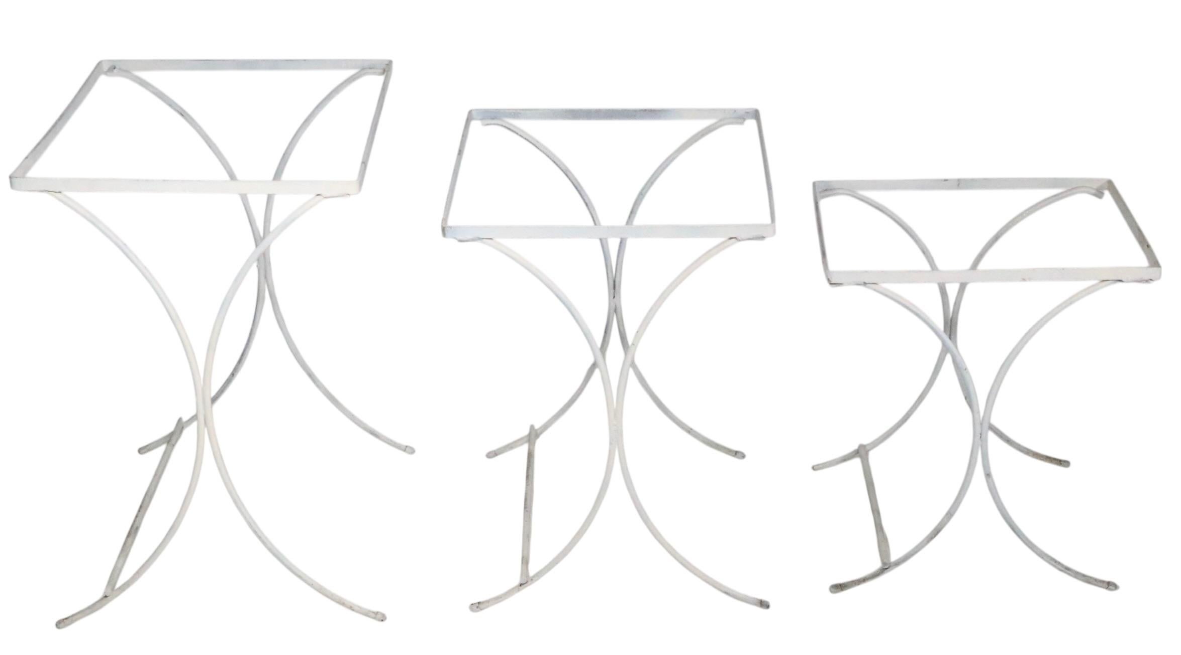 Unusual set of three  mid century nesting tables constructed of wrought iron and textured glass. The tables feature elegant intersecting curved legs, which support the rectangular tops, with original textured glass inserts. 
 Executed in the style