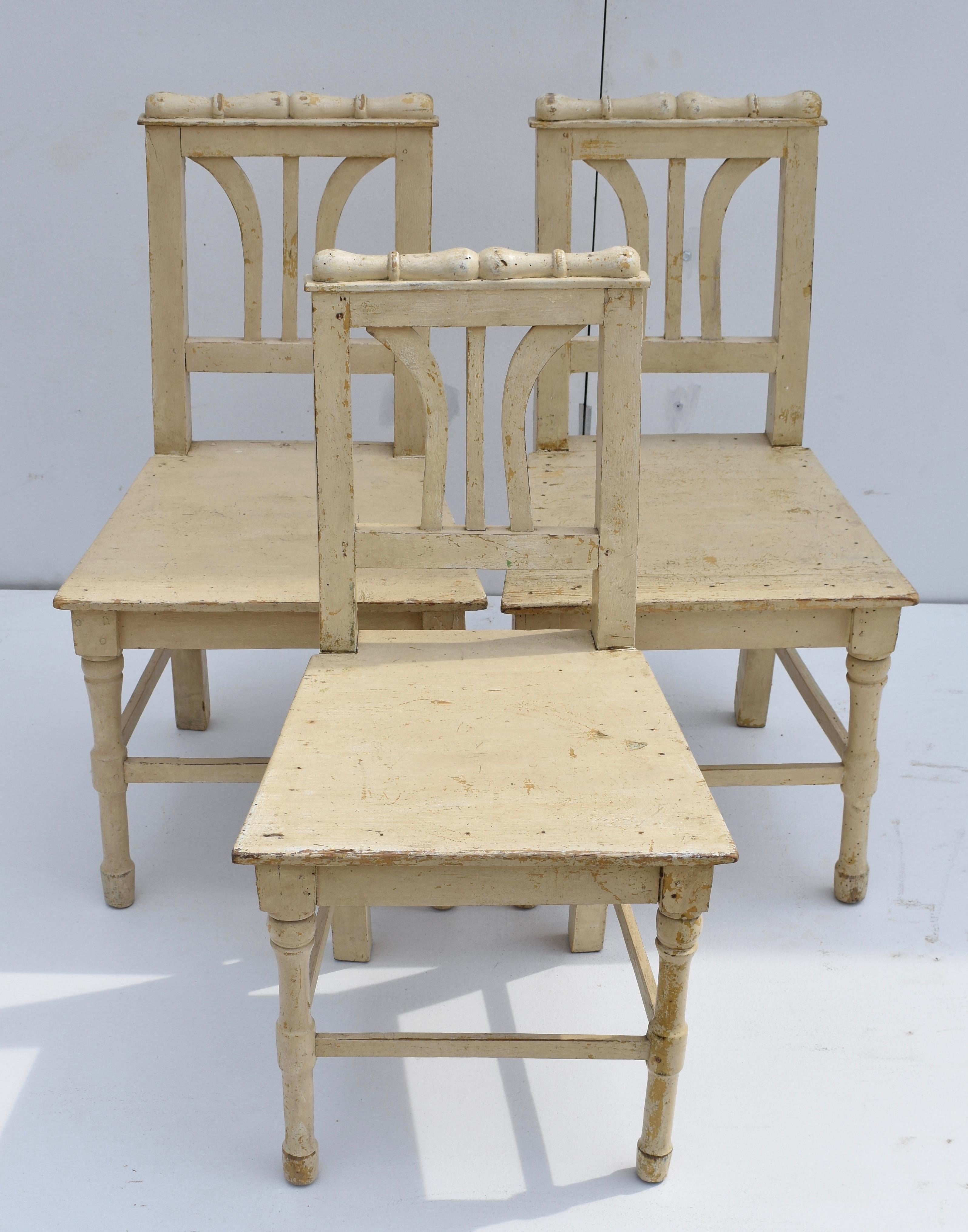These delightful plank seat children’s chairs are in a rustic Empire style, with a scroll at the top of the back rail and turned legs at the front. In old worn buttermilk paint. Seat height is 14.5