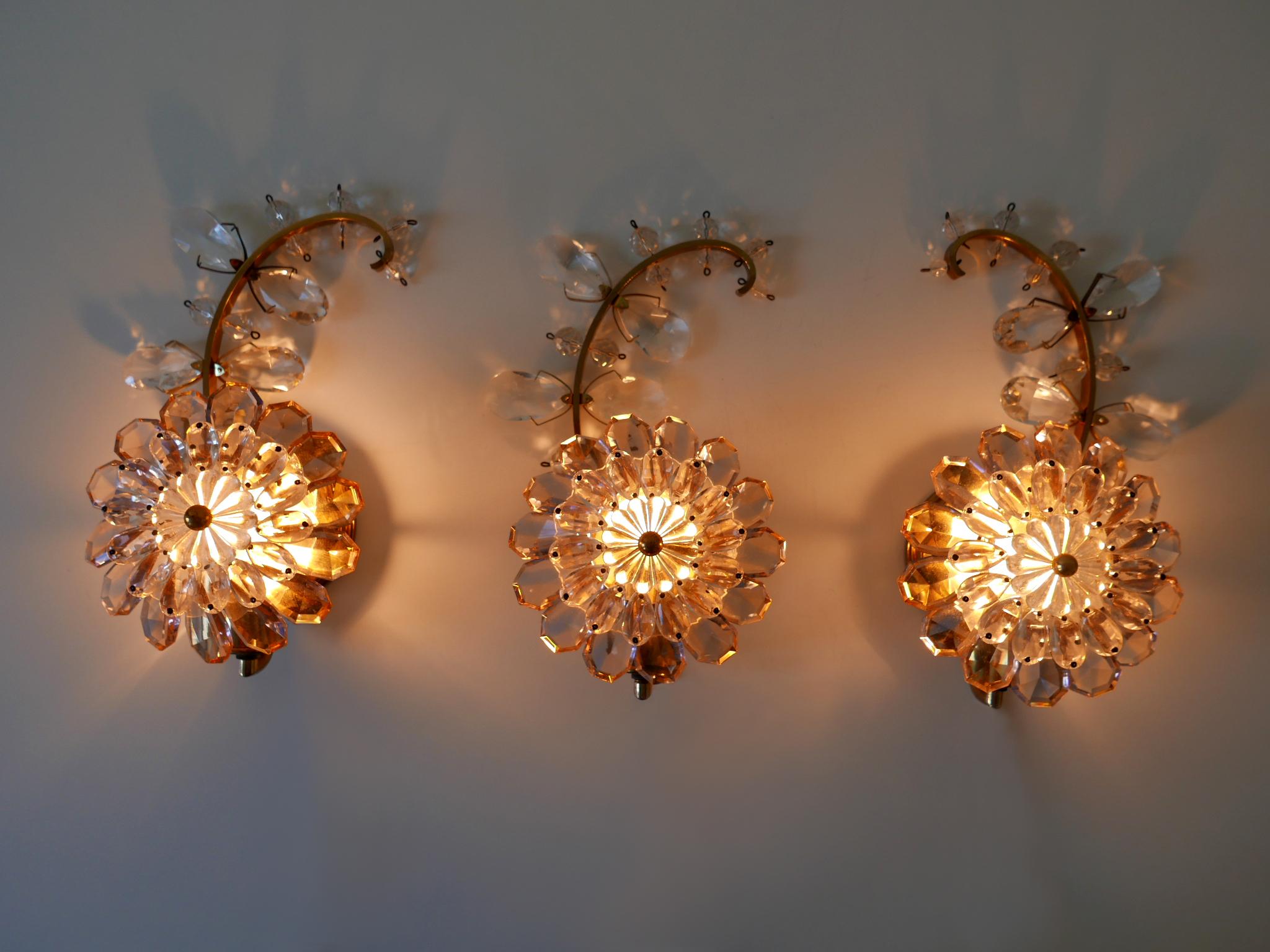 Exceptional set of three highly decorative and beautiful Mid-Century Modern iridescent crystal glass and brass flower sconces or wall lamps. Manufactured by Palwa, 1960s, Germany.

Executed in iridescent crystal glass and polished brass, each lamp