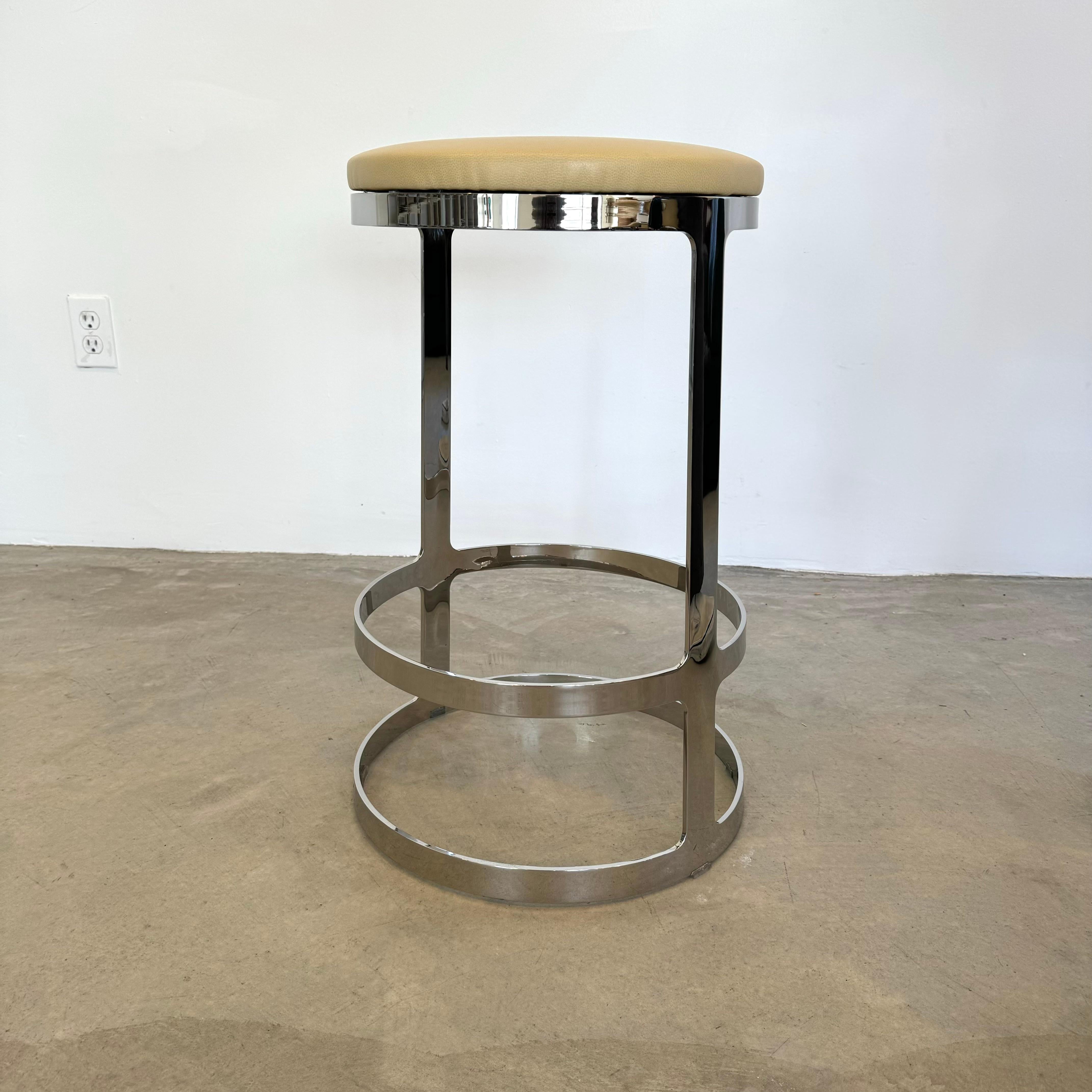 Set of three sculptural stainless steel stools with a beige leather swivel seat. Sleek and modern metal frame. The stools sit atop a circular base with two circular rungs. One ring for your feet to rest on and as the frame tapers out slightly at the