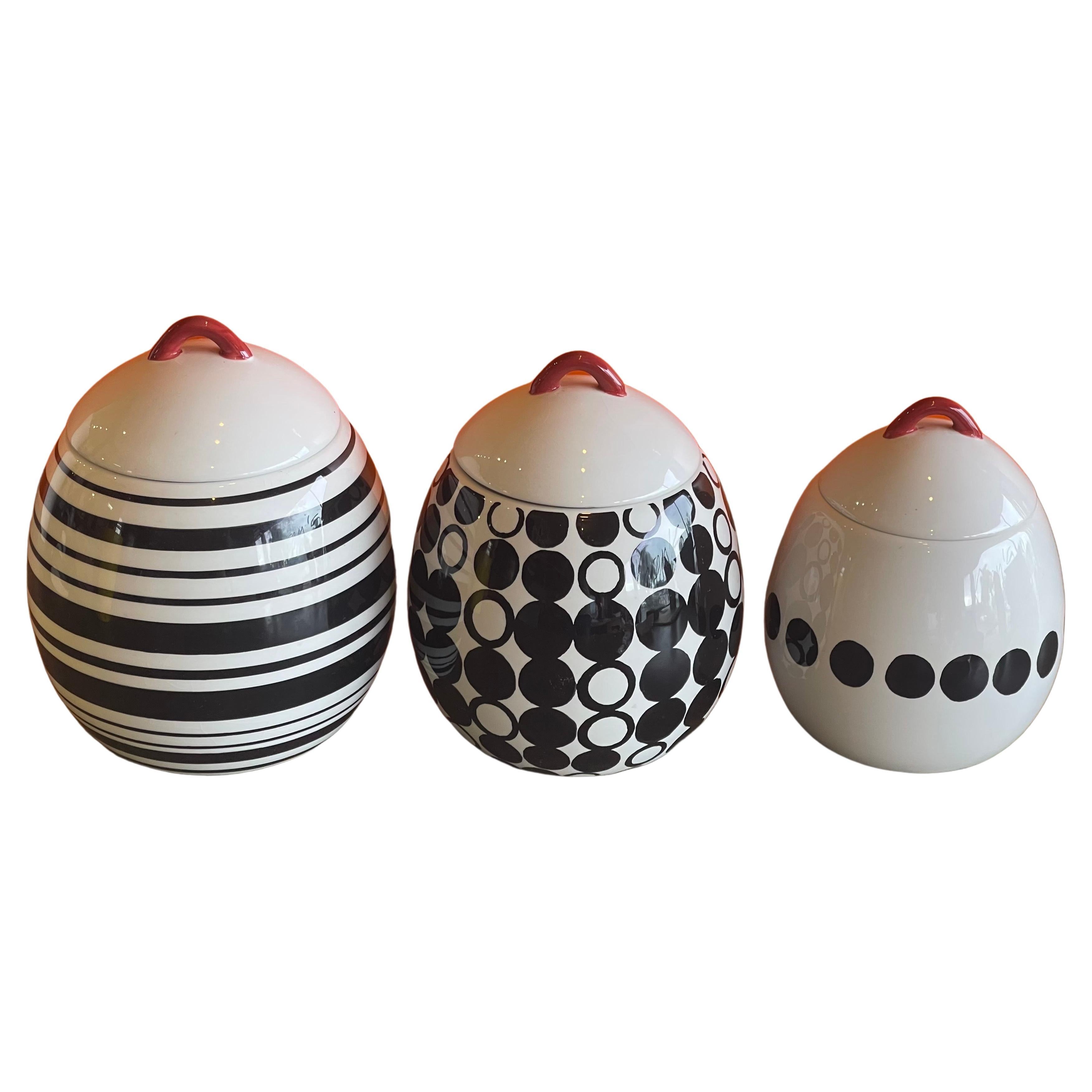 Set of three post-modern ceramic storage cannisters, circa 1990s. The cannisters are egg shaped with black and white geometric patterns and red handles on the removeable lids. The set is in good vintage condition and canisters measure: 6.5