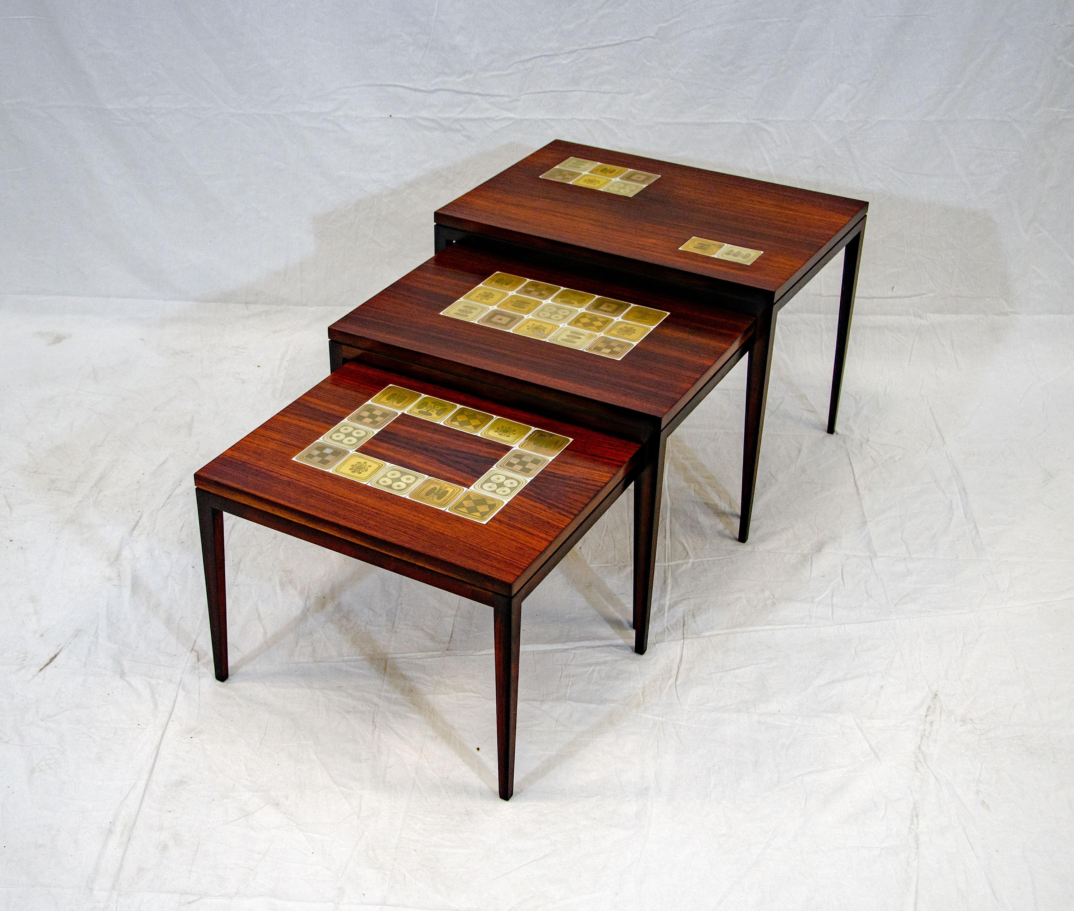 Nest of three rosewood veneer side tables on receding heights each with different arrangements of decorated patterns in gilt porcelain tiles inlays with geometric patterns. The tiles are decorated with abstracted plant motifs in different tones of