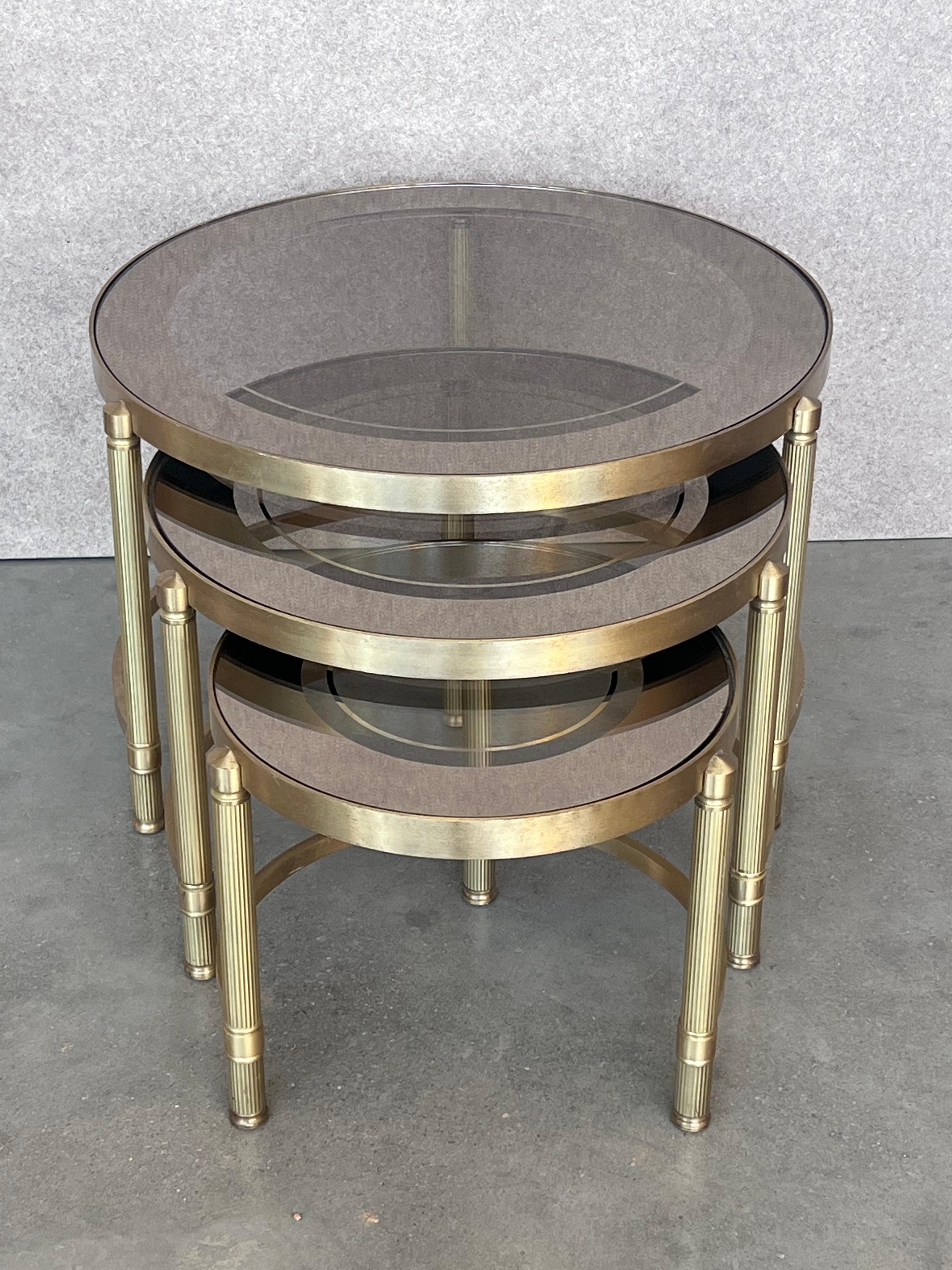 Set of three round brass nesting tables with decorative details and smoked glass tops. 

Measures: 
Small 14.75