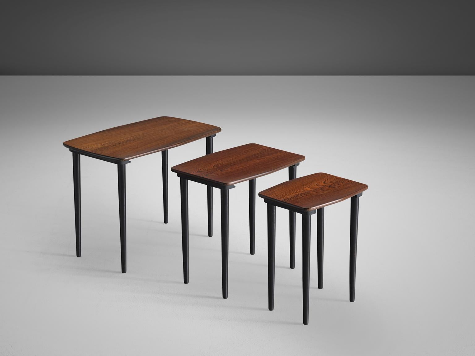 Set of three nesting tables, in dark wood, Scandinavia, 1950s.

Elegant set of three nesting tables. Each tables has a rectangular top with a soft, rounded border. The cylindrical legs are tapered with a round thickening at the end. The teak has a