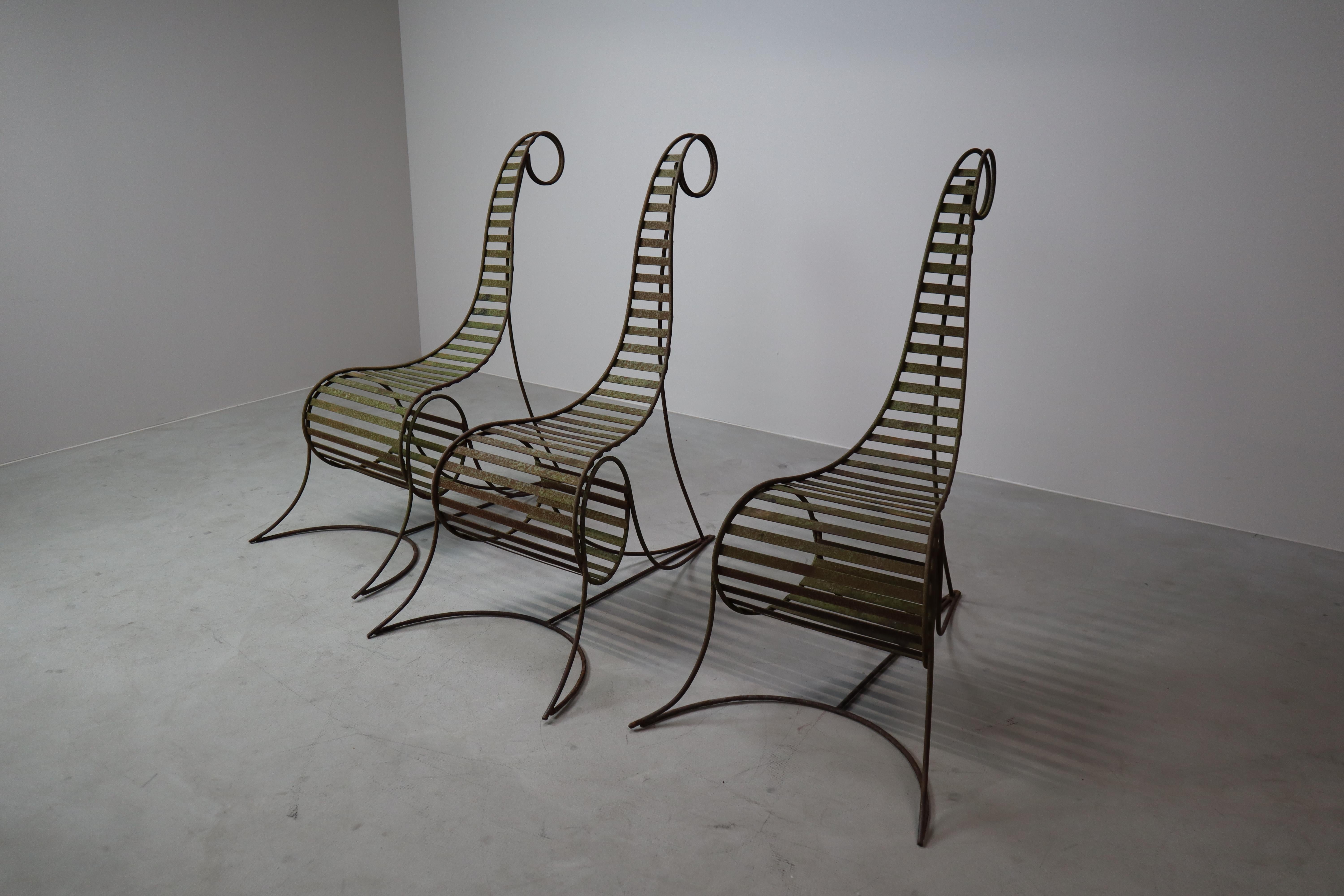 This striking set of three sculptural iron chairs features tall, spiraling backrests and a raw, expressive presence that echoes the iconic “Spine Chair” by André Dubreuil. Crafted from solid iron rods, each piece reveals a unique, hand-wrought