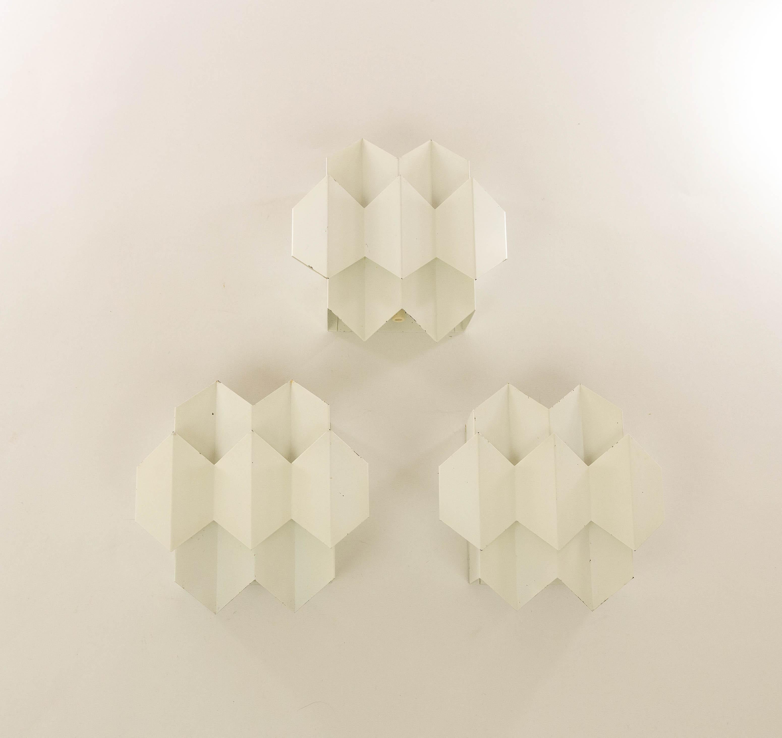 Set of three white geometrical Septet wall lamps designed by Bent Karlby and manufactured by Lyfa, Denmark.

Two layers of bent sheet metal playfully form seven hexagons, which gave the model its name: Septet. The bent layers are mounted on a