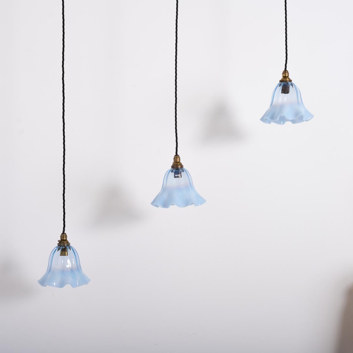 This exquisite set of three petite hand-blown vaseline glass shades showcases the artistry of Art Nouveau design. Each shade features a vibrant iridescent blue tulip shape with a delicate frilled edge that graduates to a milky opaline finish.
The
