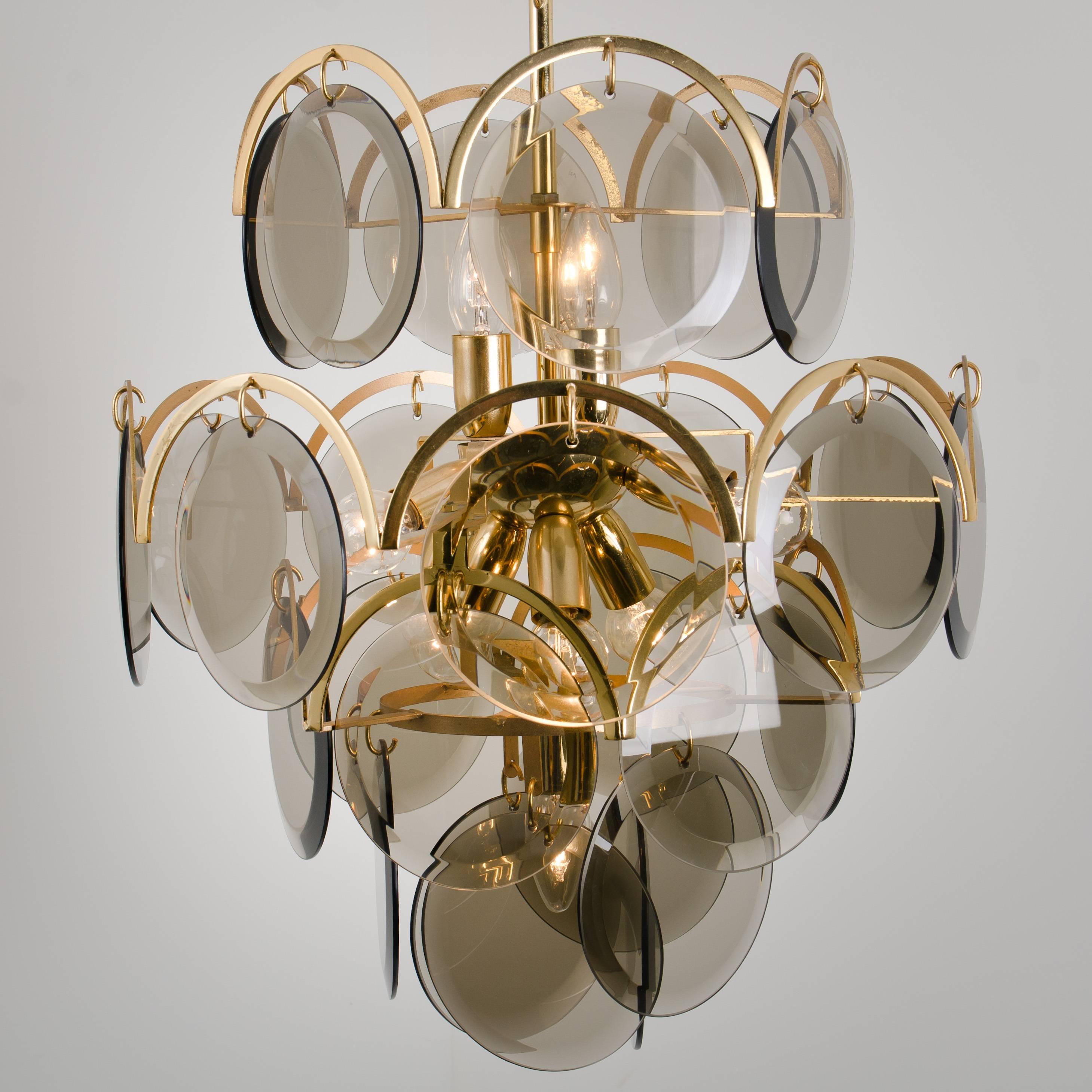 A set of three gorgeous hanging light fixtures, attributed to Vistosi with graduated tiers of smoked round facet chapped glass discs framed by half moon shaped brass. The chandeliers are complete, no hook or glass disk is missing, with its original