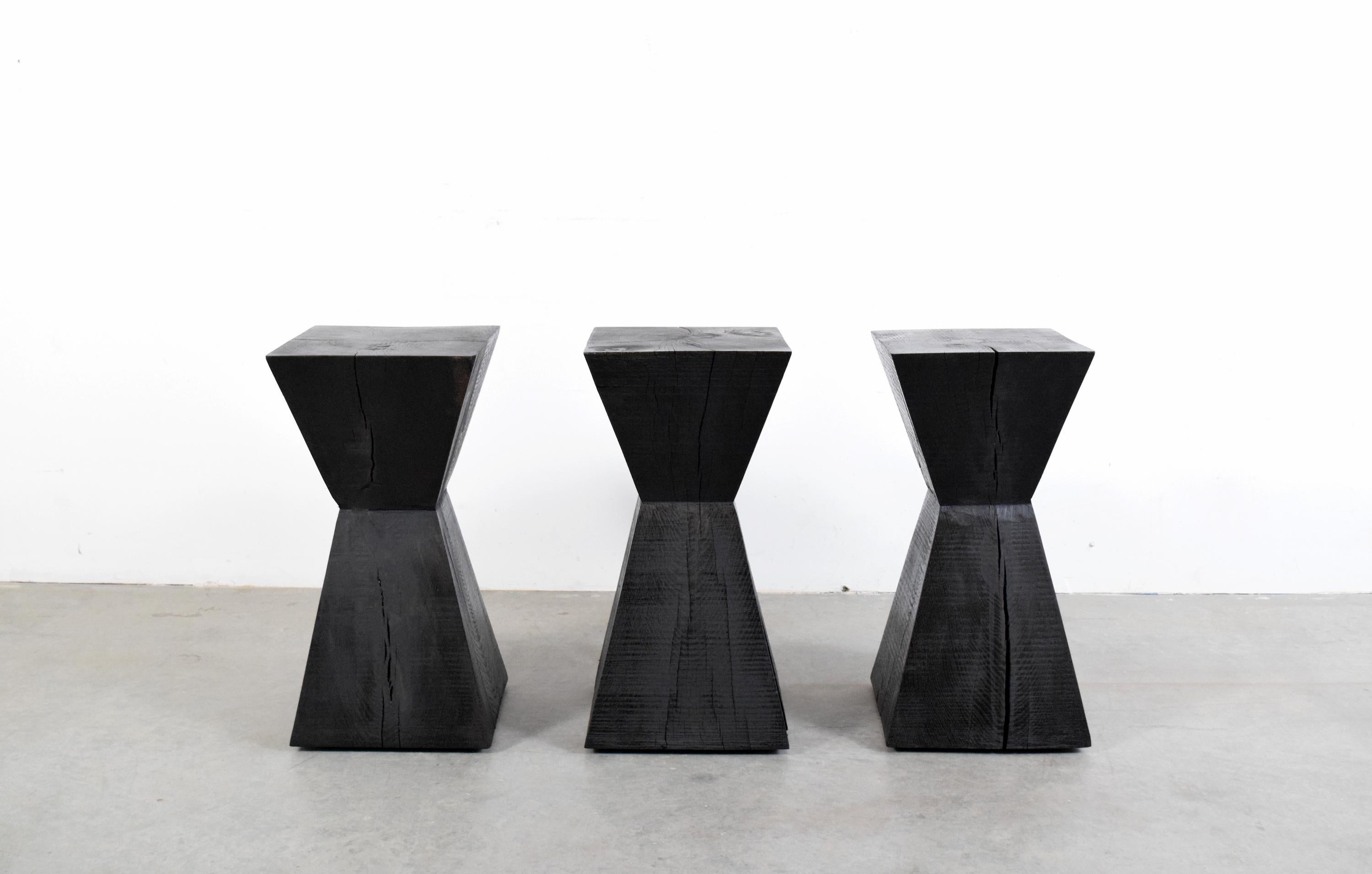 Set of three solid, ebonized, rough hewn, oak pedestal tables in the manner of French Interior Designer Christian Liaigre. Most likely produced in the late 1980s, or early 1990s, each piece is cut from a solid piece of oak, and therefore exhibit