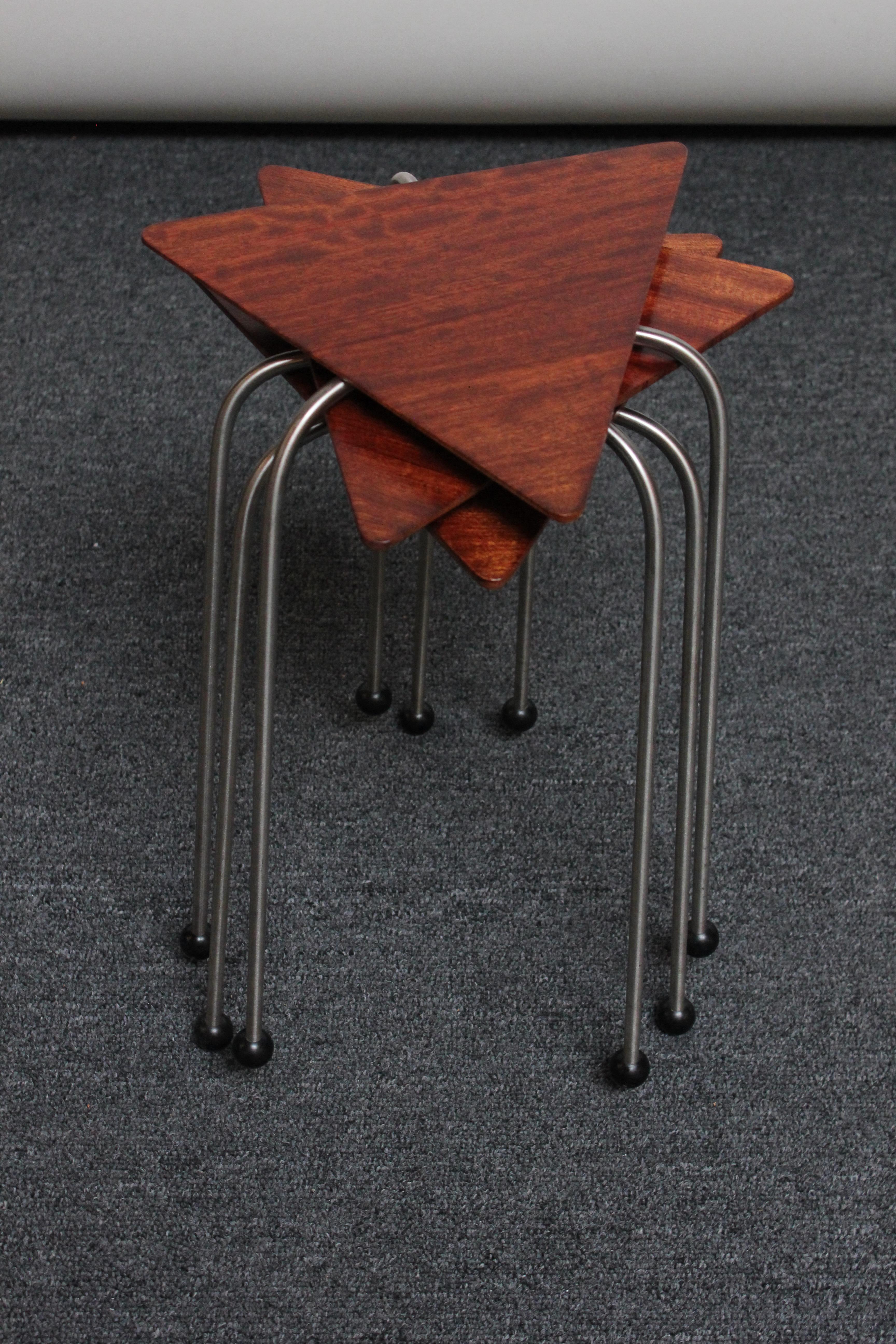 Sculptural stacking tables by contemporary designer, David Kiernan (ca. 1990s, USA). Composed of solid bubinga triangular tops supported by tripod steel rod bases with black orb feet. 
Measures: Triangle tops are 11