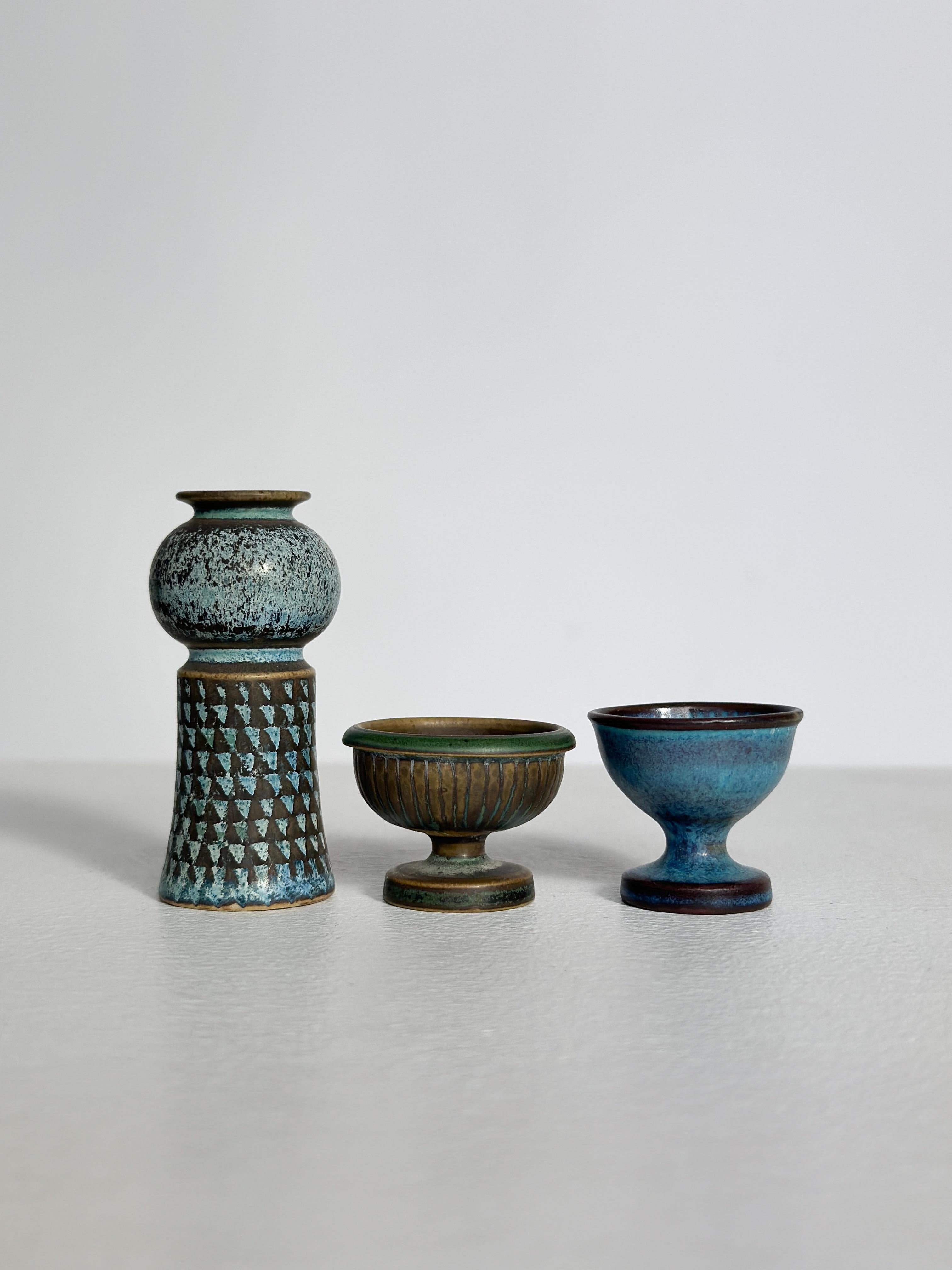 Conjunto de tres jarrones y vasijas en miniatura únicos de Stig Lindberg para Gustavsberg en Suecia en la década de 1960.
Gres artesanal esmaltado en diferentes tonos de azul.

Jarrón alto: H 6,3 cm, 1964
Vasija marrón turquesa con rayas en el