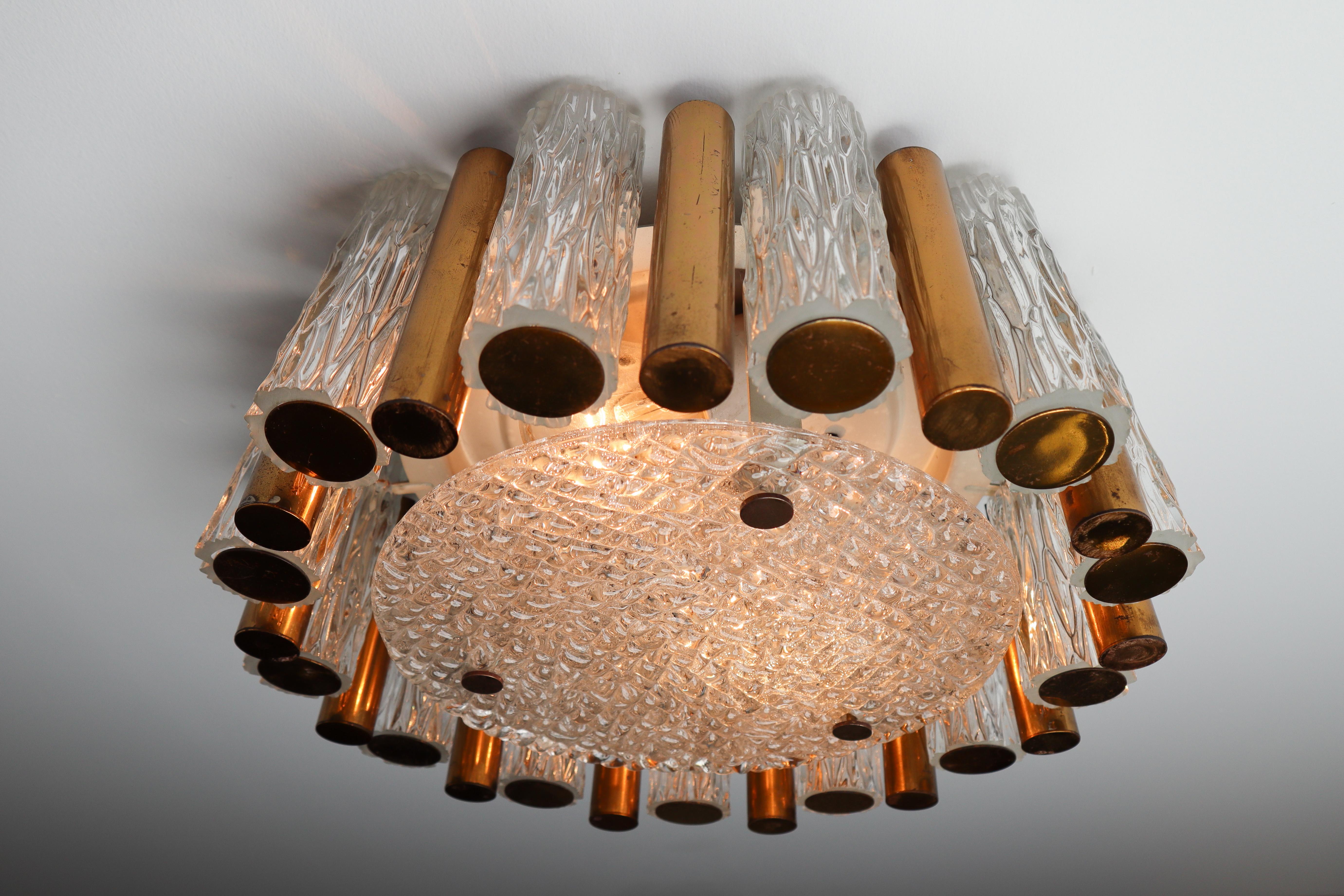 Set of three textured ice glass flush mount light fixture by Kaiser Leuchten. Round steel frame festooned alternately with glass and brass tubes and a heavy glass plate on the button. Fitted with two porcelain E27 sockets. Brass part with patina.