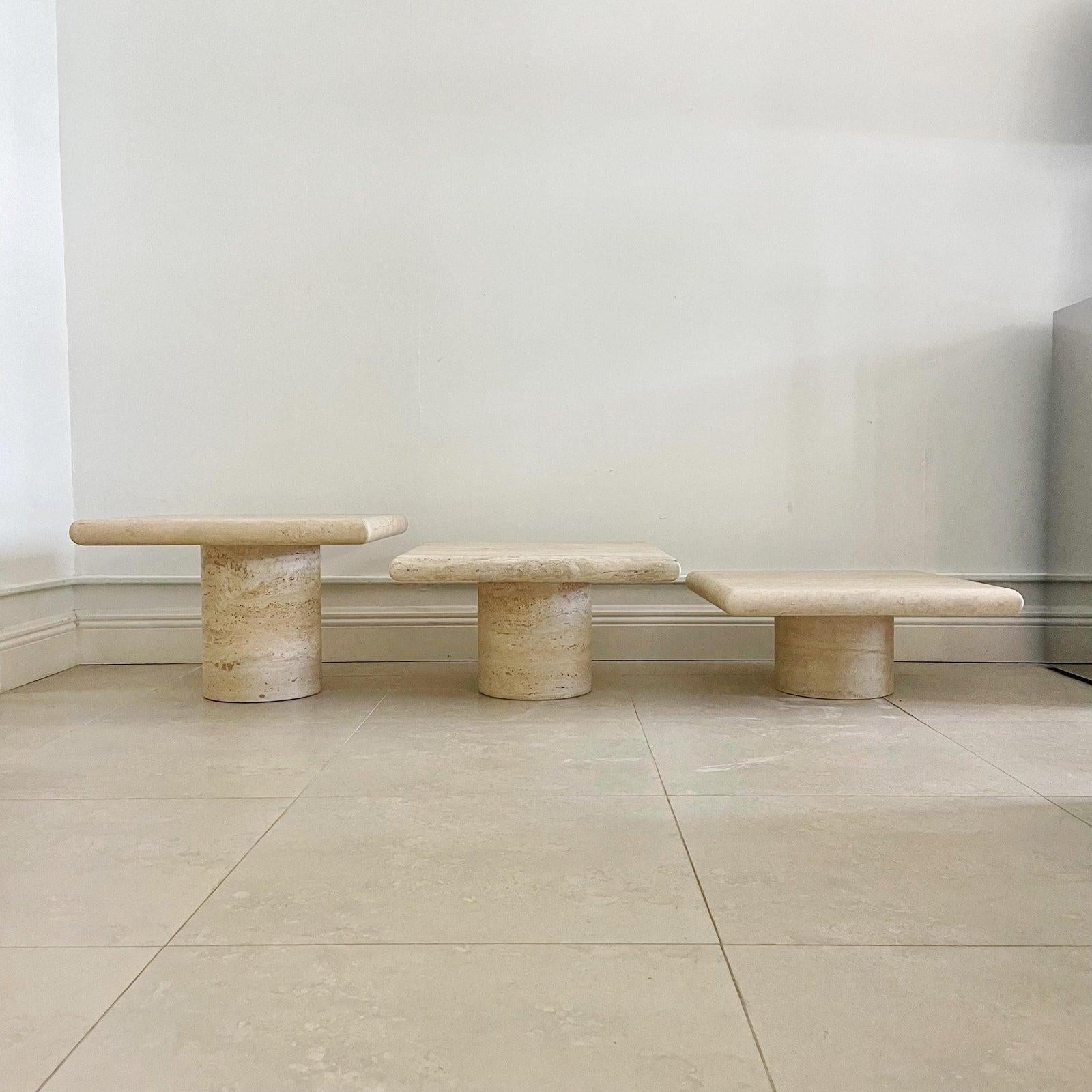 Set of three nesting tables in graduating sizes by Up & Up, Italy. Each one having a square top and cylindrical base in travertine. 
Measurements: Small Table 21.25