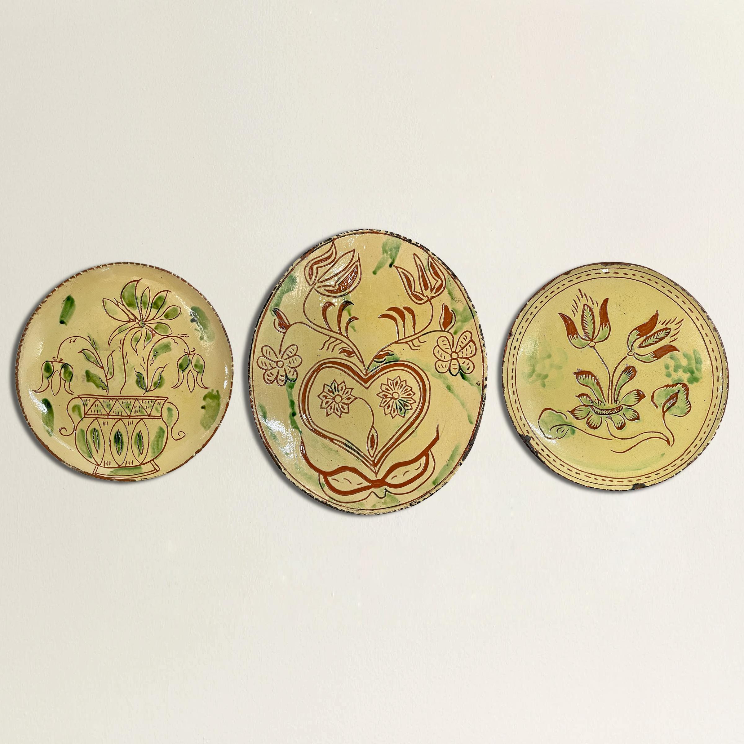A charming set of three glazed redware pottery plate reproductions by the Turtlecreek Potters of Morrow, Ohio, each decorated with incised flowers and heats and glazed in yellow and green glazes. These pieces were created in the 1980s and 90s by