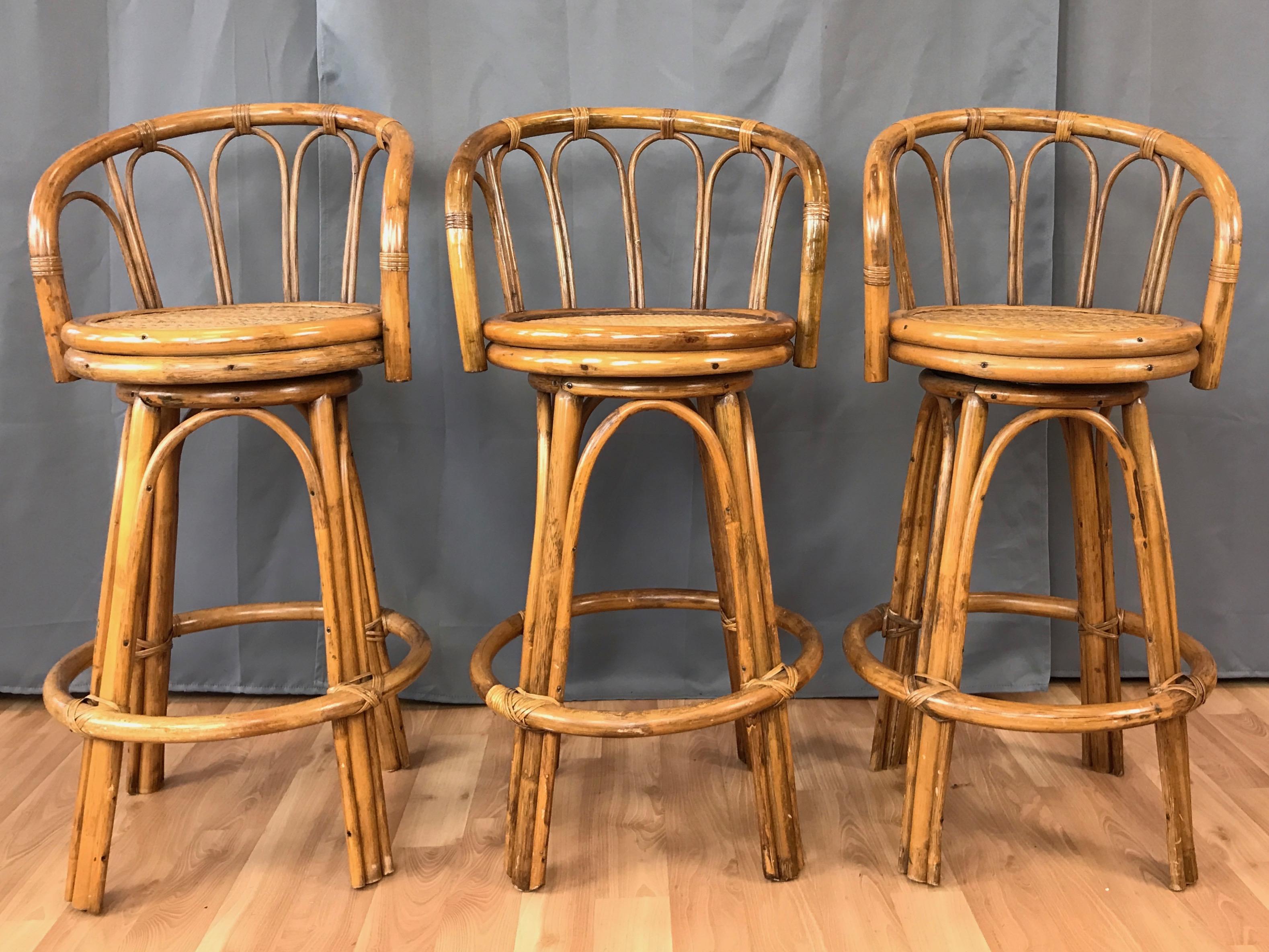 A set of three late 1960s-early 1970s bamboo and rattan swivel bar or counter stools.

Exceptionally well-crafted of bent bamboo with a 360-degree swivel seat. Rattan-wrapped joinery details throughout. Displays a handsome hint of natural patina