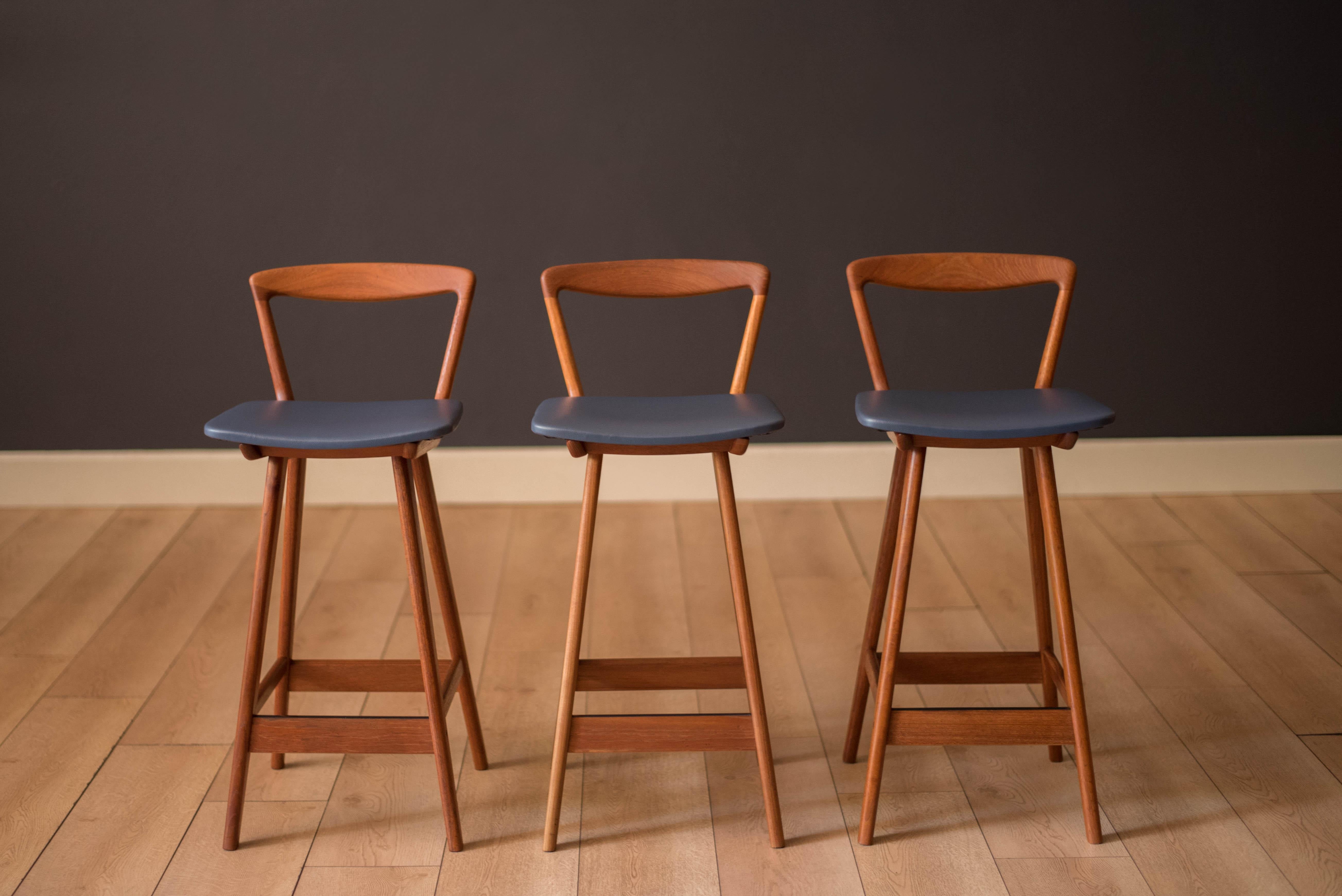 Mid-Century Modern set of three counter bar stools designed by Henry Rosengren Hansen for Brande Mobelfabrik, Denmark. Features a sculptural solid teak frame including a backrest and footrest support. This set has been professionally reupholstered