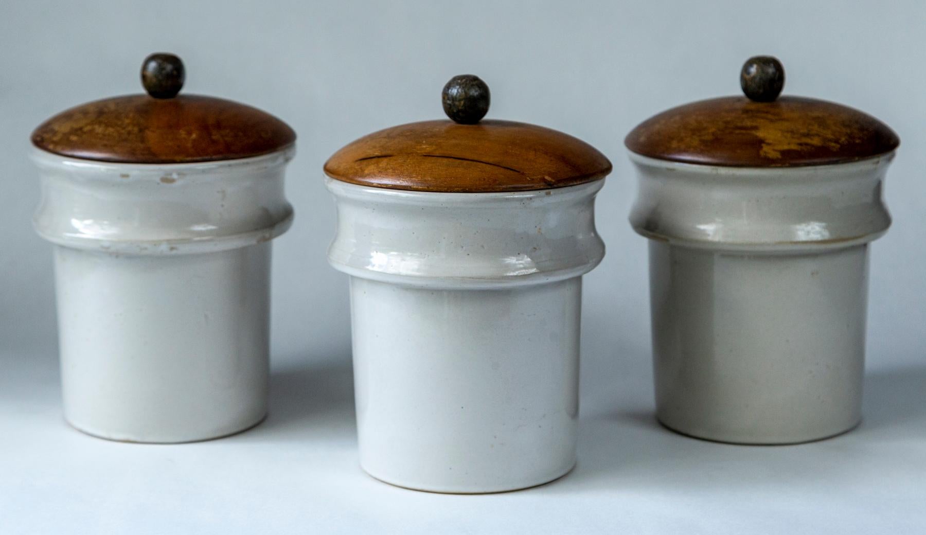 Set of three vintage ironstone apothecary jars, France, circa 1930. Wood lids cover heavy ironstone jars.