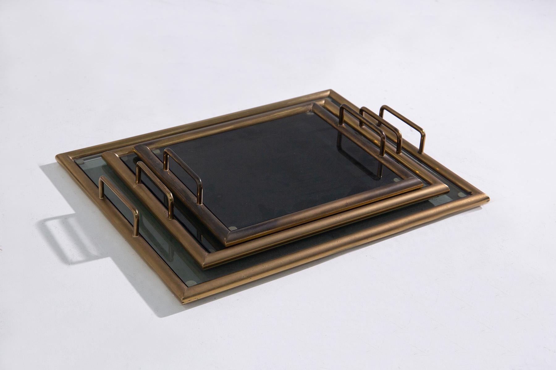 These vintage 1950s Italian-made trays exude timeless elegance and sophistication. Crafted with sturdy brass frames and topped with transparent dark smoked glass, each tray epitomizes luxury and refinement. The inclusion of brass handles enhances