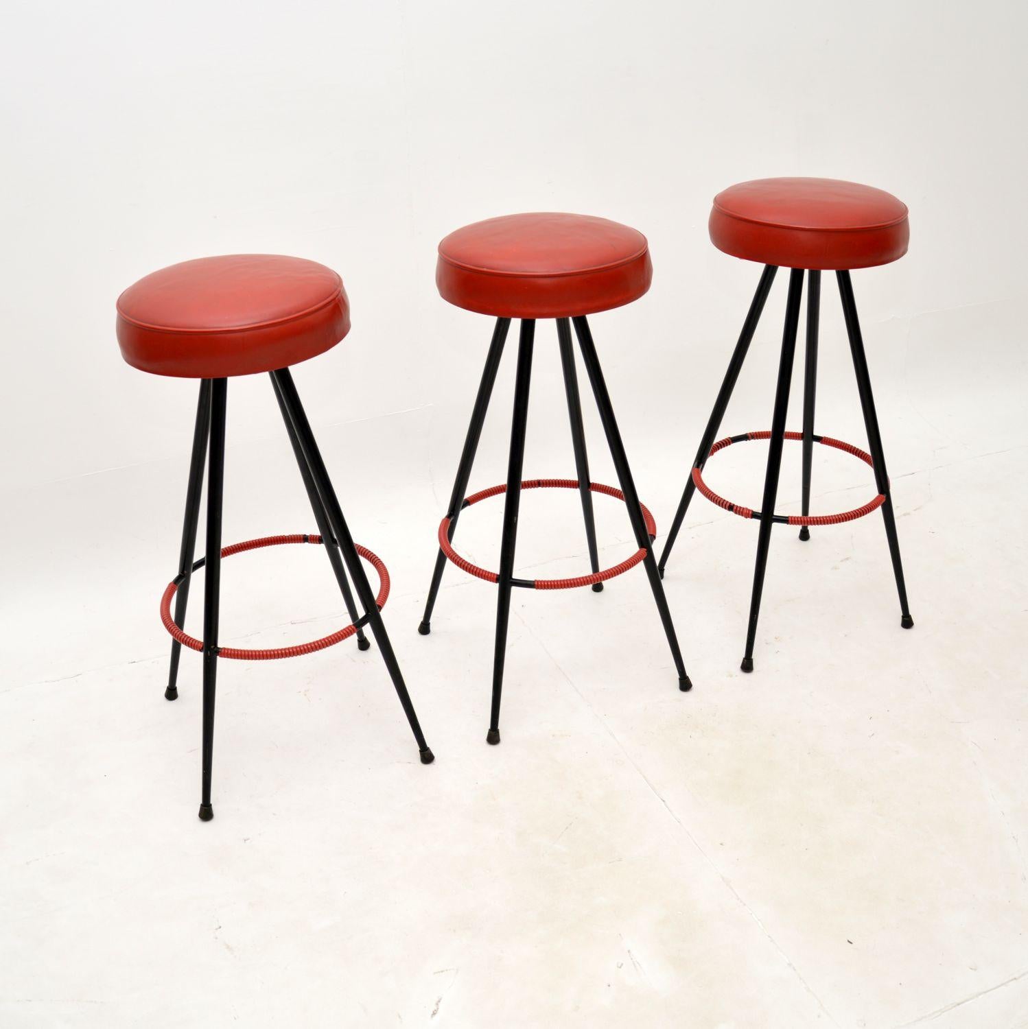 A stylish and very well made set of three vintage steel bar stools. They were made in England, they date from the 1950’s.

The quality is superb, they are beautifully designed with gorgeous red vinyl seats and red woven cord on the foot rests. The