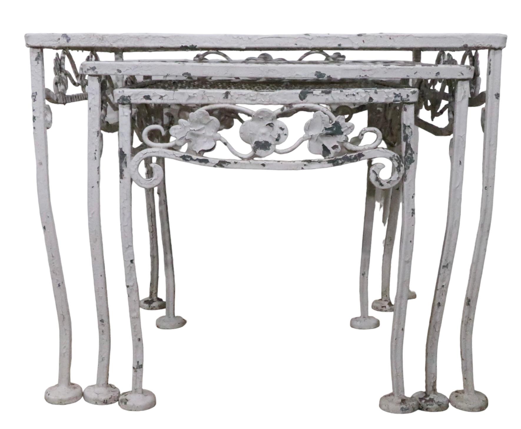 Charming set of three wrought iron nesting tables with decorative foliate trim, wrought legs, and metal mesh tops. The tables are structurally sound and sturdy, free of breaks, bends or repairs. The paint finish shows wear, peeling , loss etc.