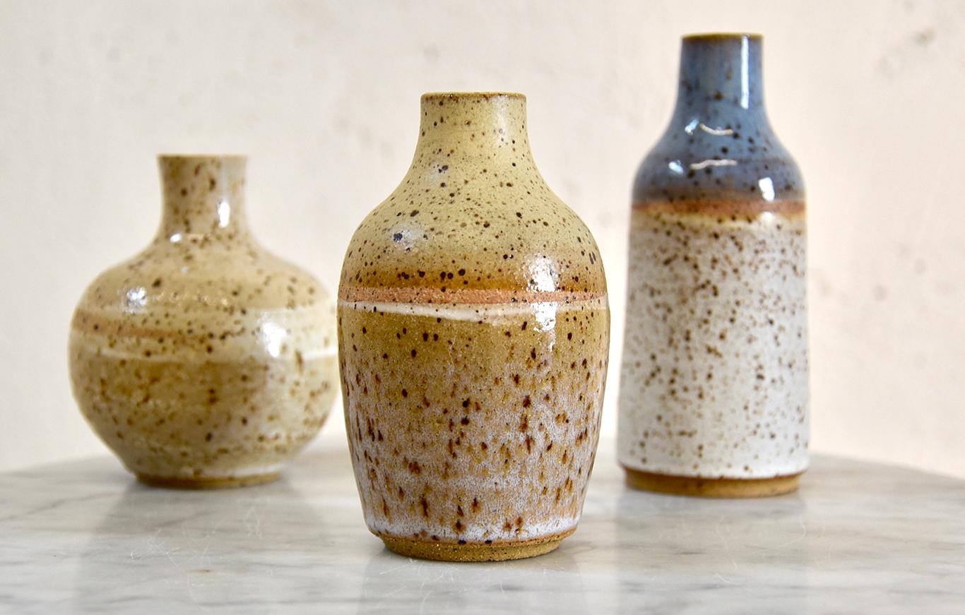 Signe Yberg's stunning set of three wheel thrown mini-bottles are made from a speckled buff stoneware and glazed in a contemporary neutral palette of a muted light blue, creams and goldenrod with rust accents. 

The largest bottle measures 4