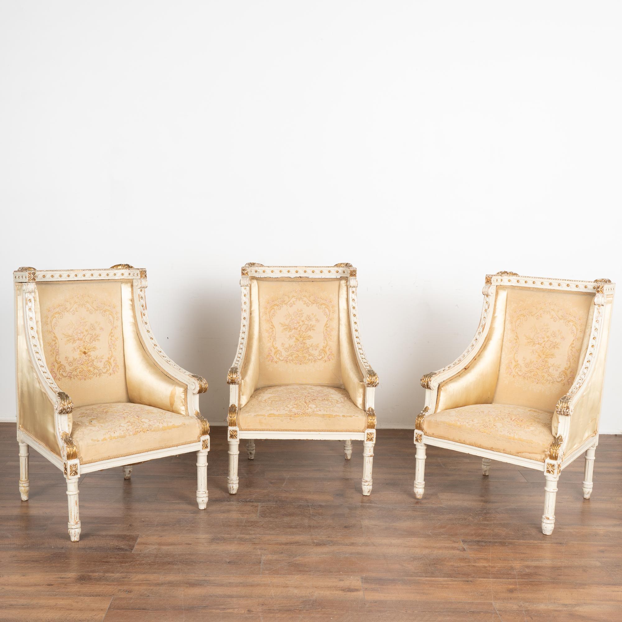 Set of three upholstered arm chairs from France with original white painted finish accented with gold trim.
Carved details throughout include acanthus leaves, braided trim with bead detail, turned fluted legs, and medallion accents.
Wood frame is