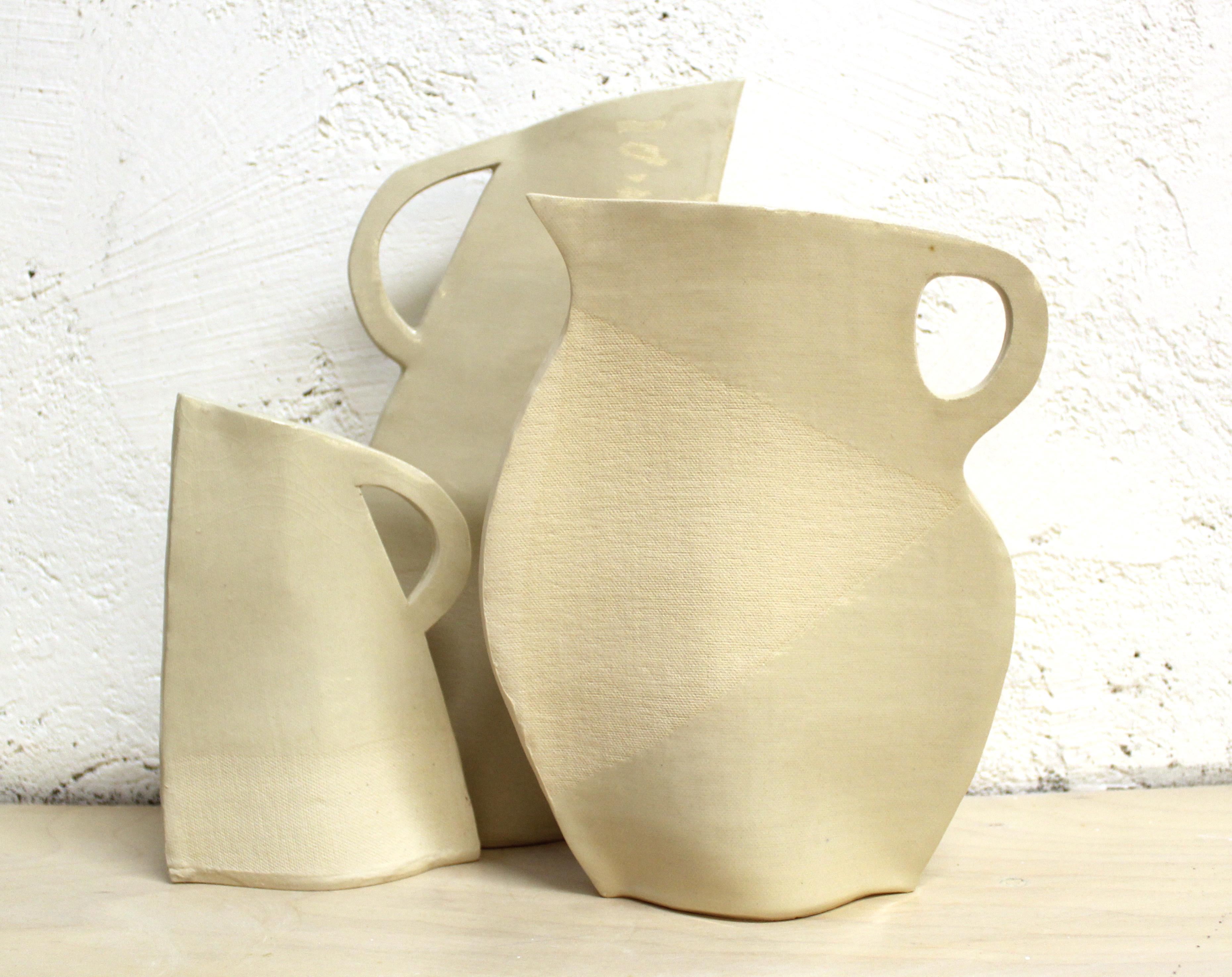 This set of three flat vases by Alison Owen is made through Owen's skillful hand-building technique, utilizing thin slabs of white stoneware clay, partially dipped in clear glaze to create a subtle textural and surface design. The canvas texture of