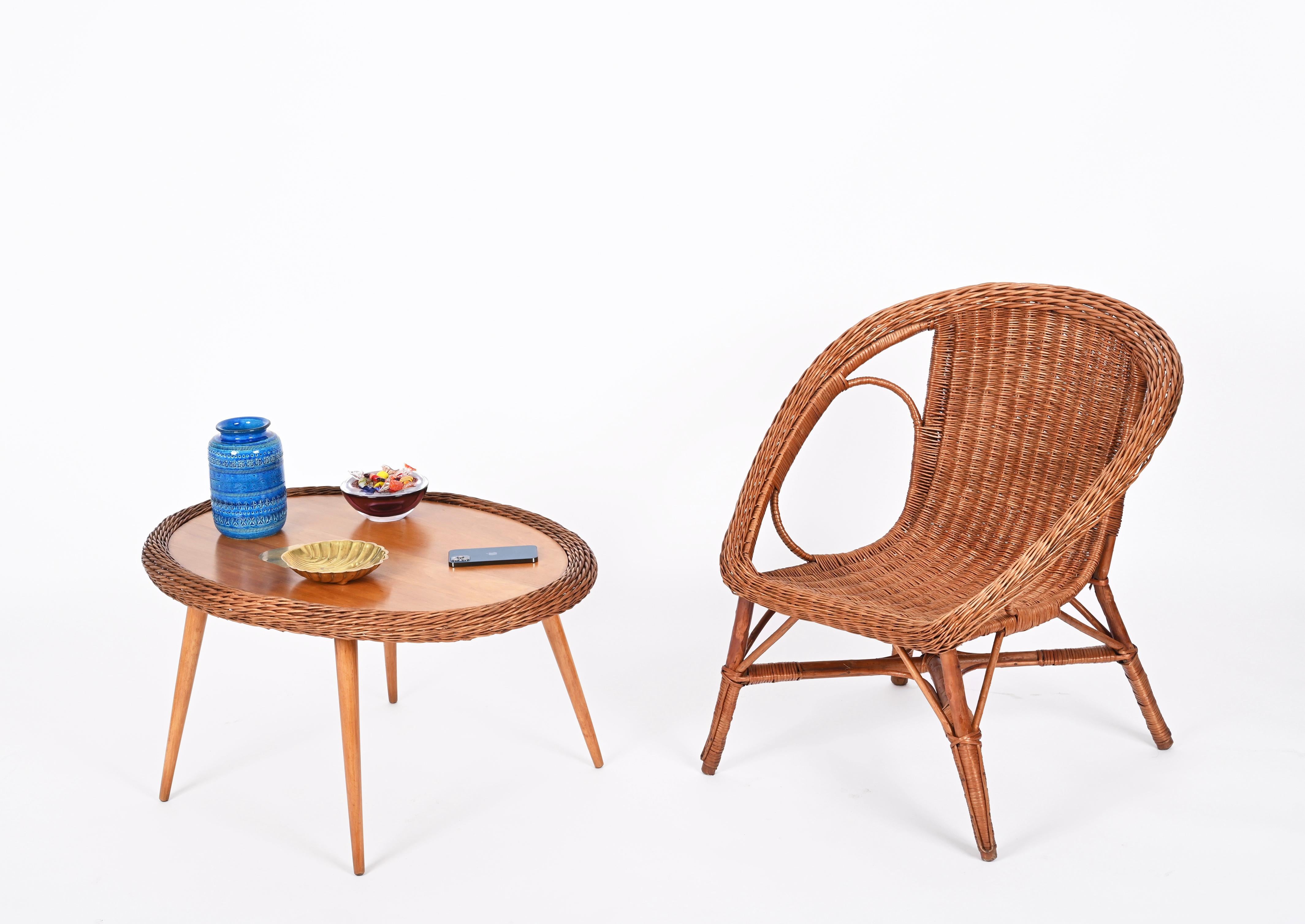 Fabulous midcentury wicker and wood table and chair set. This fantastic set is in the style of Tony Paul and made in Italy in the 60s.

This unique set consists of three armchairs in hand-woven wicker and an oval coffee table that features a top