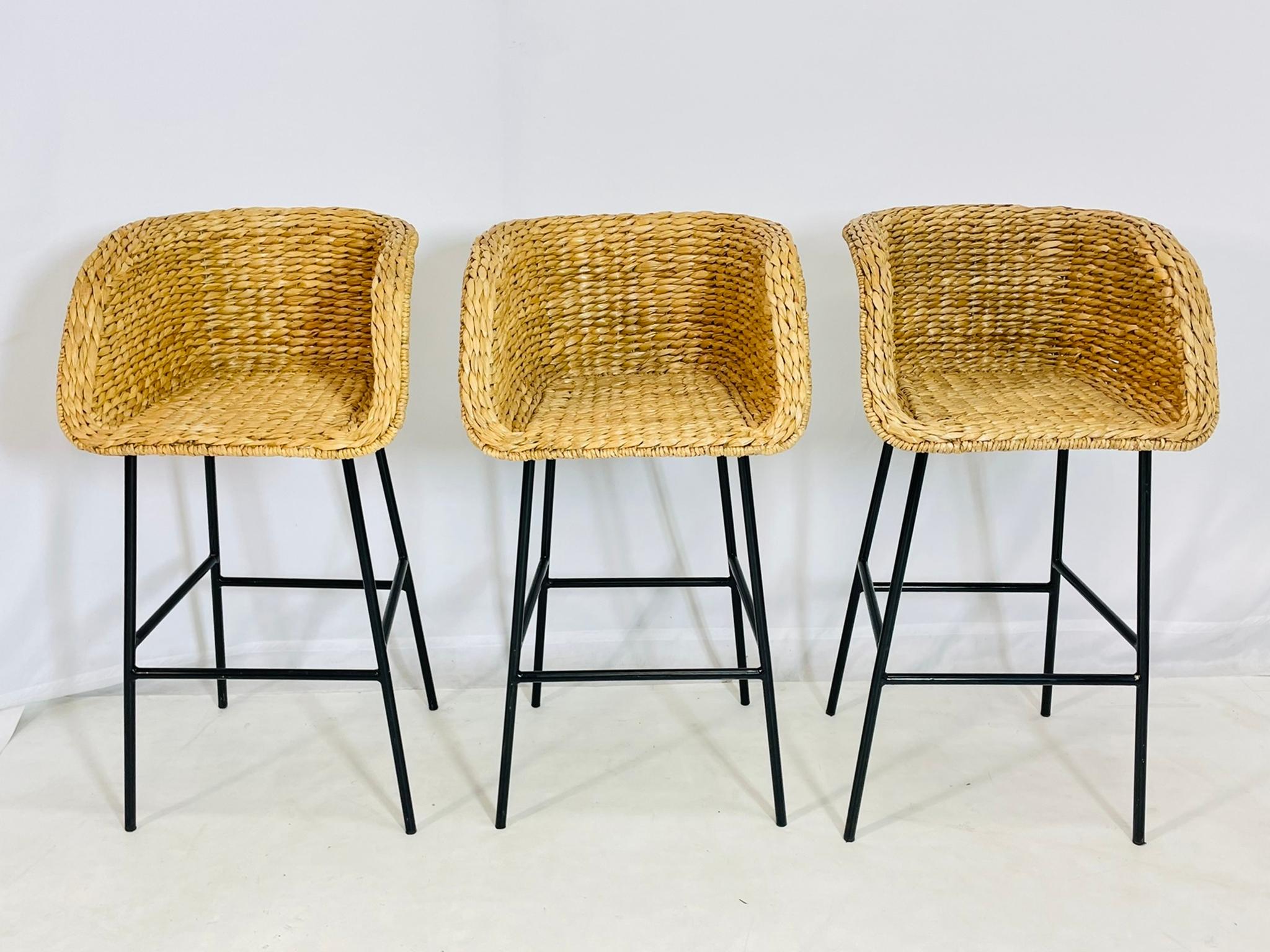 Dieses stilvolle Set aus drei modernen Barhockern mit handgeflochtenen Wasserhyazinthen-Sitzen auf minimalistischen schwarzen Metallfüßen wertet Ihre Küche oder Ihren Barbereich auf. Jeder Hocker verfügt über eine anmutig geschwungene Rückenlehne,