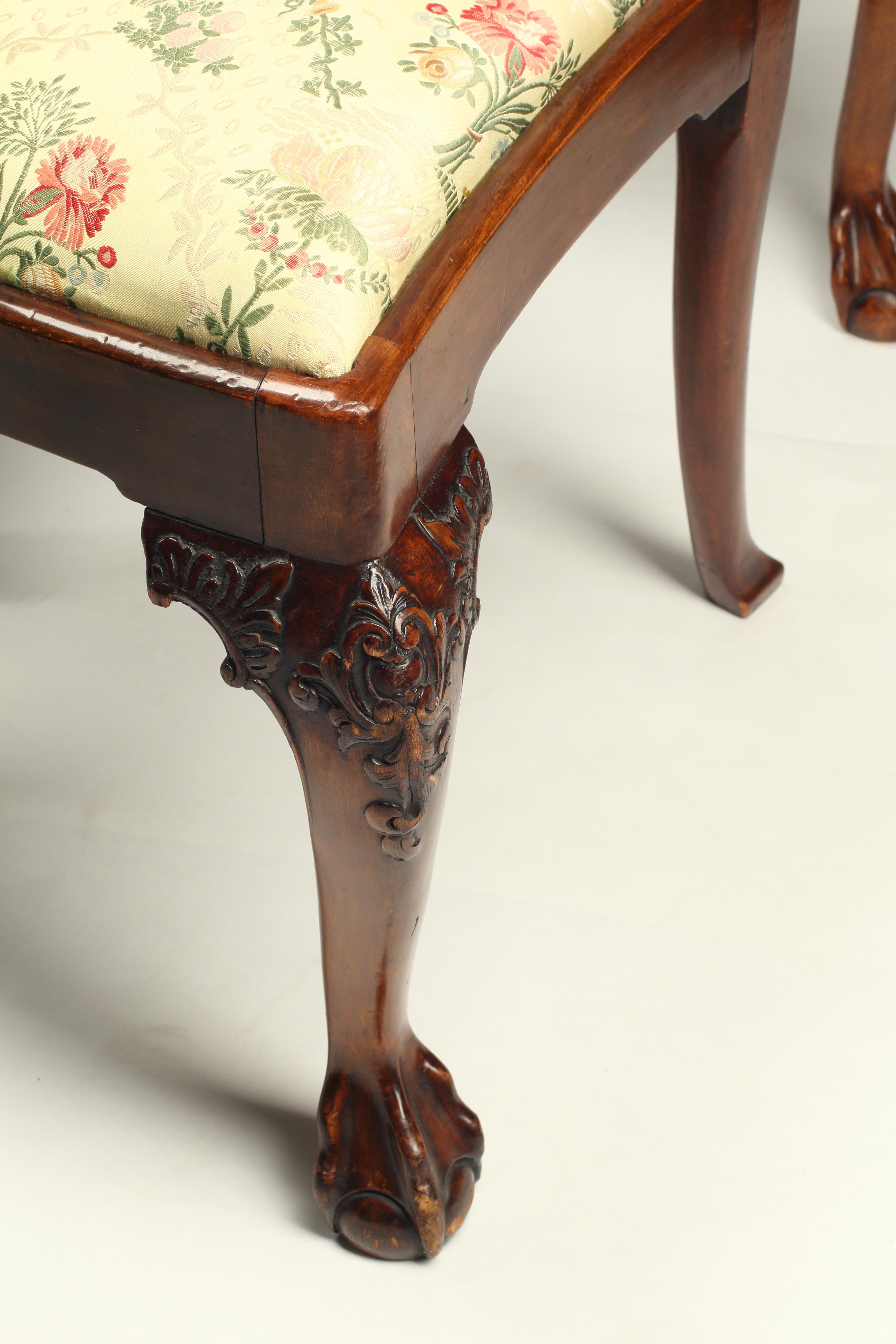 Questo imponente set di dodici sedie da pranzo in stile Chippendale comprende due poltrone e dieci sedie laterali, tutte meticolosamente realizzate e intagliate a mano in mogano. Gli schienali intricati sono caratterizzati da impressionanti motivi a