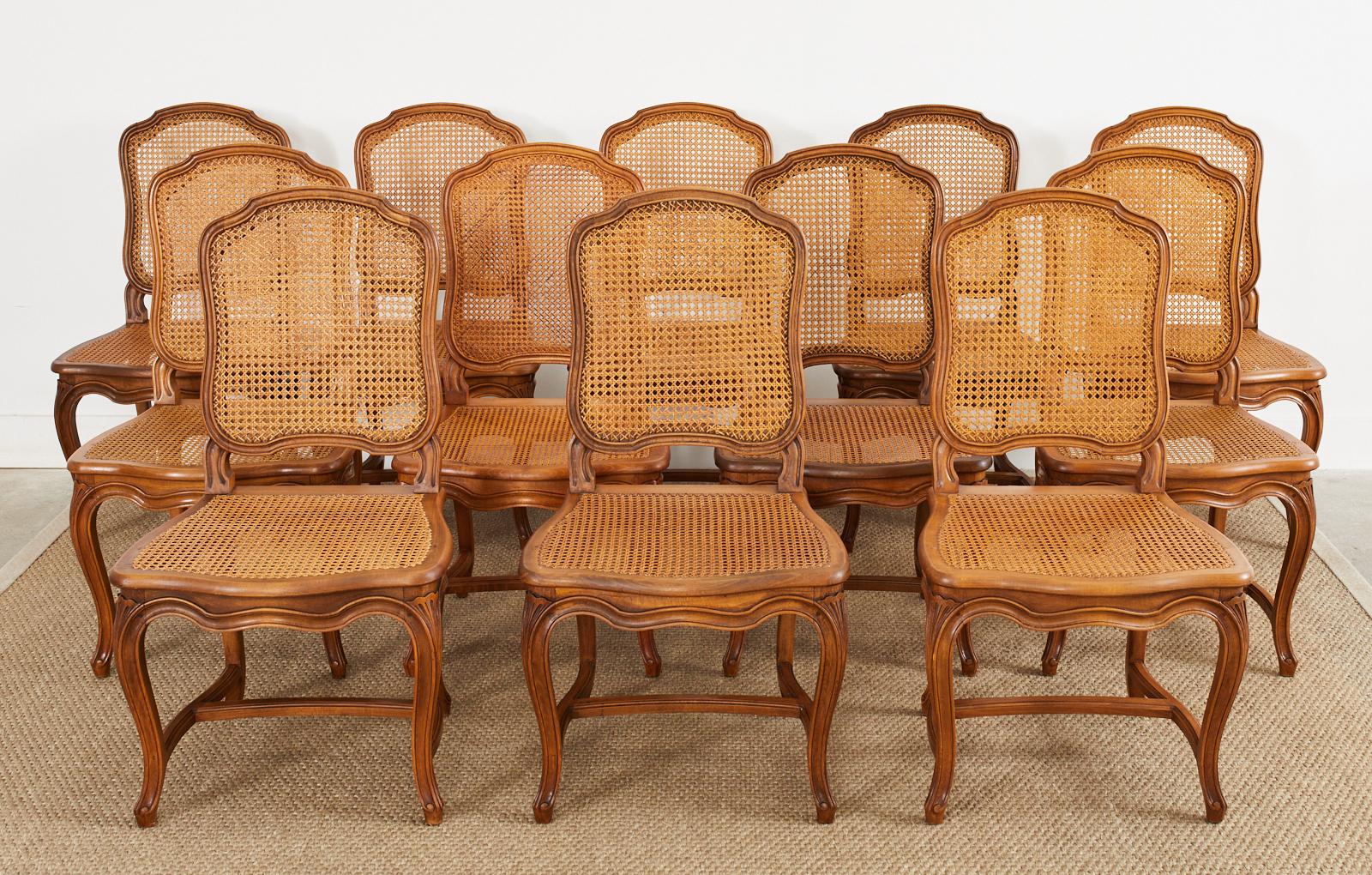 Remarkable set of twelve hand-crafted French dining chairs constructed from fruitwood. Made in the country French provincial taste featuring caned seats and backs. The shaped back conjoins to a seat with serpentine shaped aprons supported by