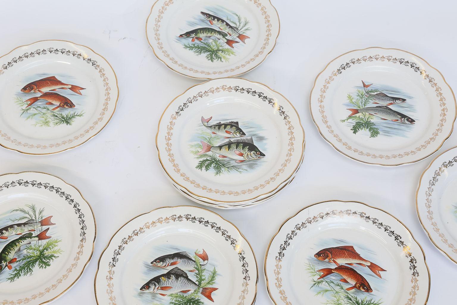 This is a set of twelve Digoin & Sarreguemines porcelain plates. The plates are transfer printed with six different designs of swimming fish with a gilt border. There are two plates of each of the six designs. The gilt mark on the back of the plates