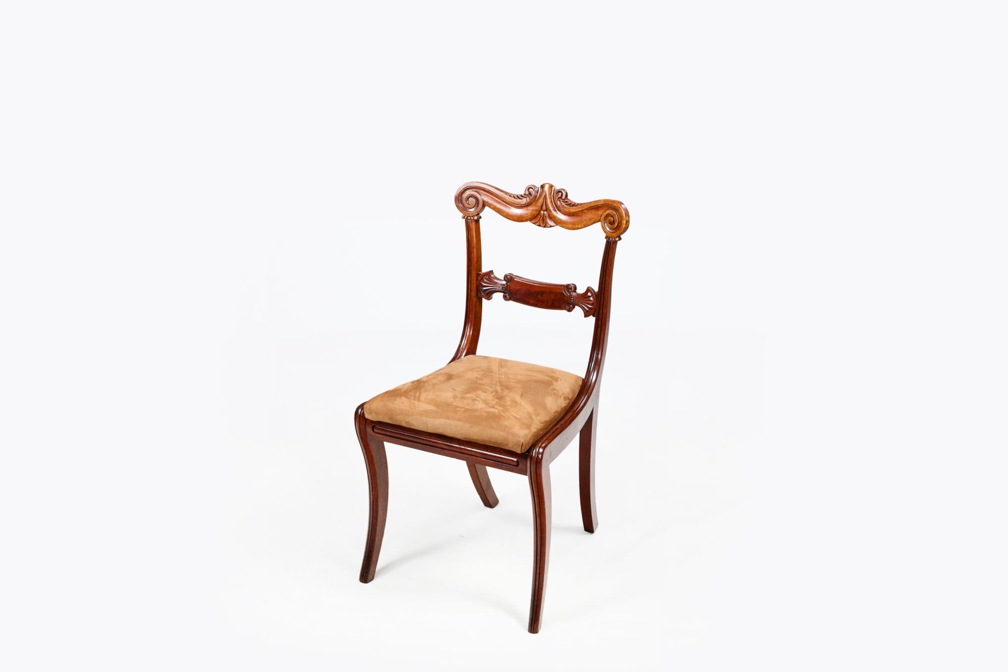 Set di dodici sedie da pranzo Regency in mogano dell'inizio del XIX secolo con dettaglio a volute intagliate sulla sponda superiore, dettaglio a ventaglio intagliato sulle stecche orizzontali e gambe a sciabola. Tra cui una coppia di intagliatori