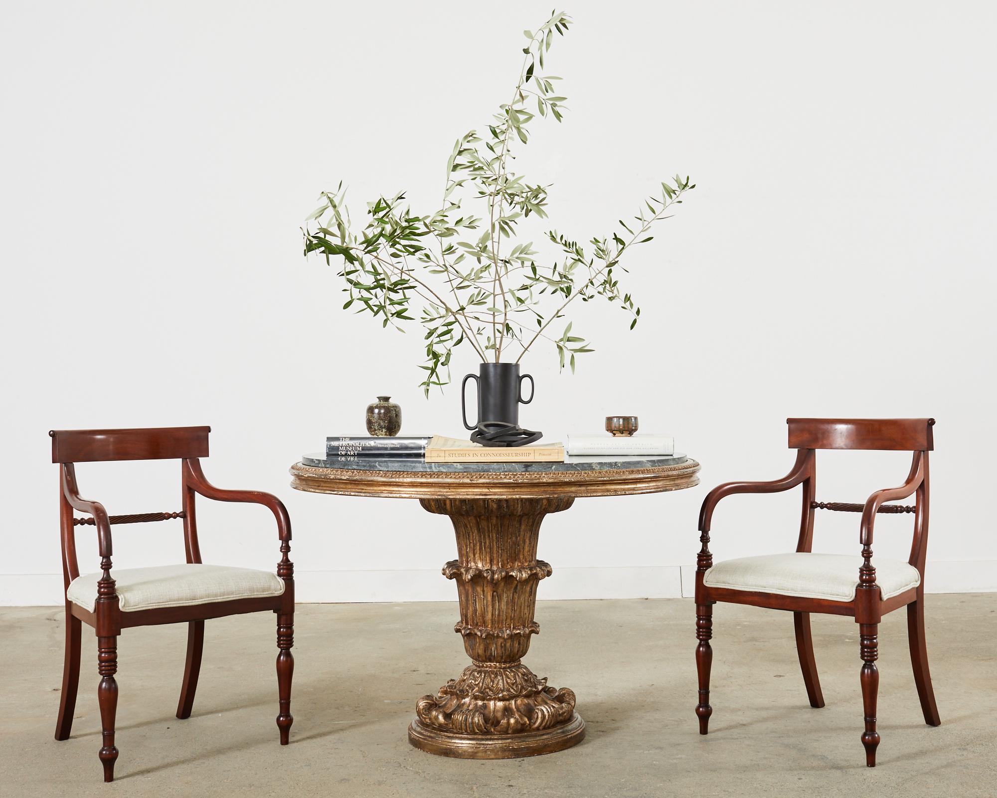 Grand set of twelve mahogany dining chairs made in the English regency taste. The deep mahogany frames have a Greek klismos inspired tablet back that gracefully curves down the back to saber legs. The set consists of  10 side chairs and two host