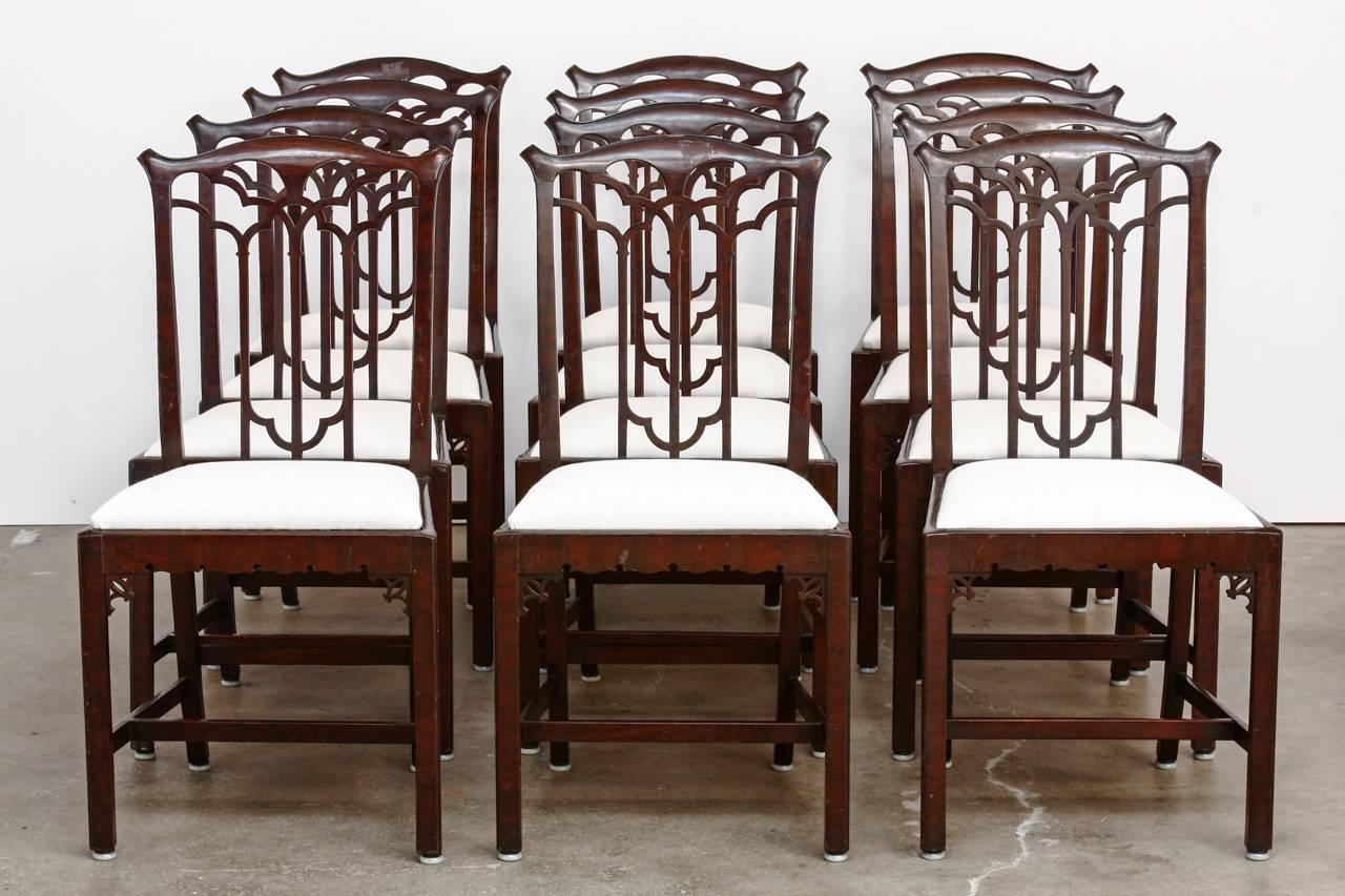 Rare set of 12 English Victorian dining chairs made in the Gothic Revival taste of the early 19th century by Hamptons of Pall Mall London, England. Constructed from mahogany with peaked crests and Gothic style splats and spandrels. Newly refurbished