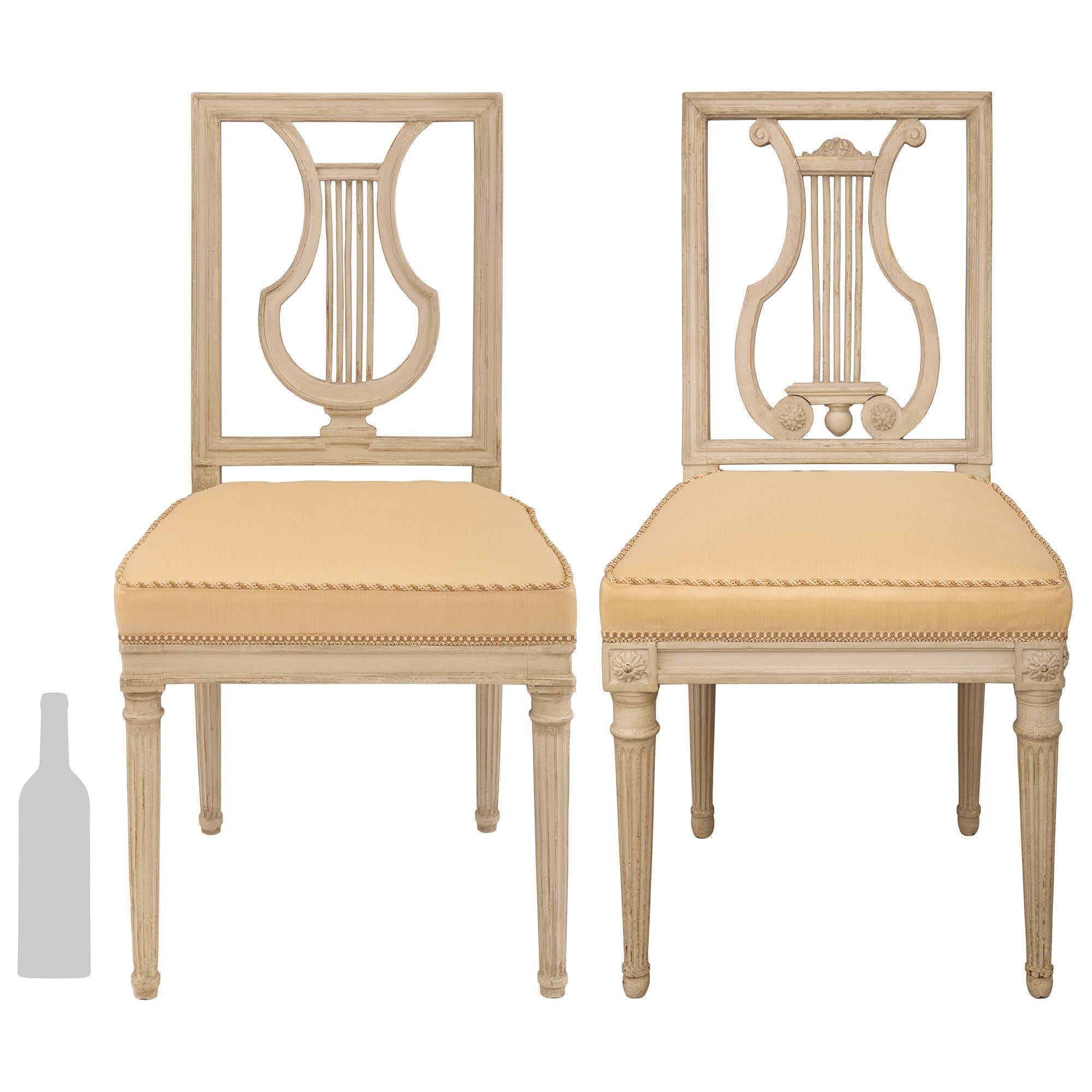 Ein sehr eleganter Satz von zwölf französischen Esszimmerstühlen aus dem 18. Jahrhundert im Stil Louis XVI. Jeder patinierte grau/cremefarbene Stuhl steht auf runden, konisch zulaufenden, kannelierten Beinen mit geschnitzten Bändern oben und unten.