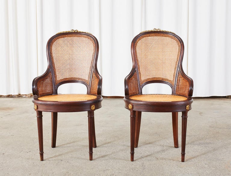 Extraordinary 19th century set of twelve French mahogany dining chairs crafted in the grand Louis XVI taste. The large set of chairs feature a caned seat, back, and double caned arms. Graceful mahogany frames having a rounded back with a decorative