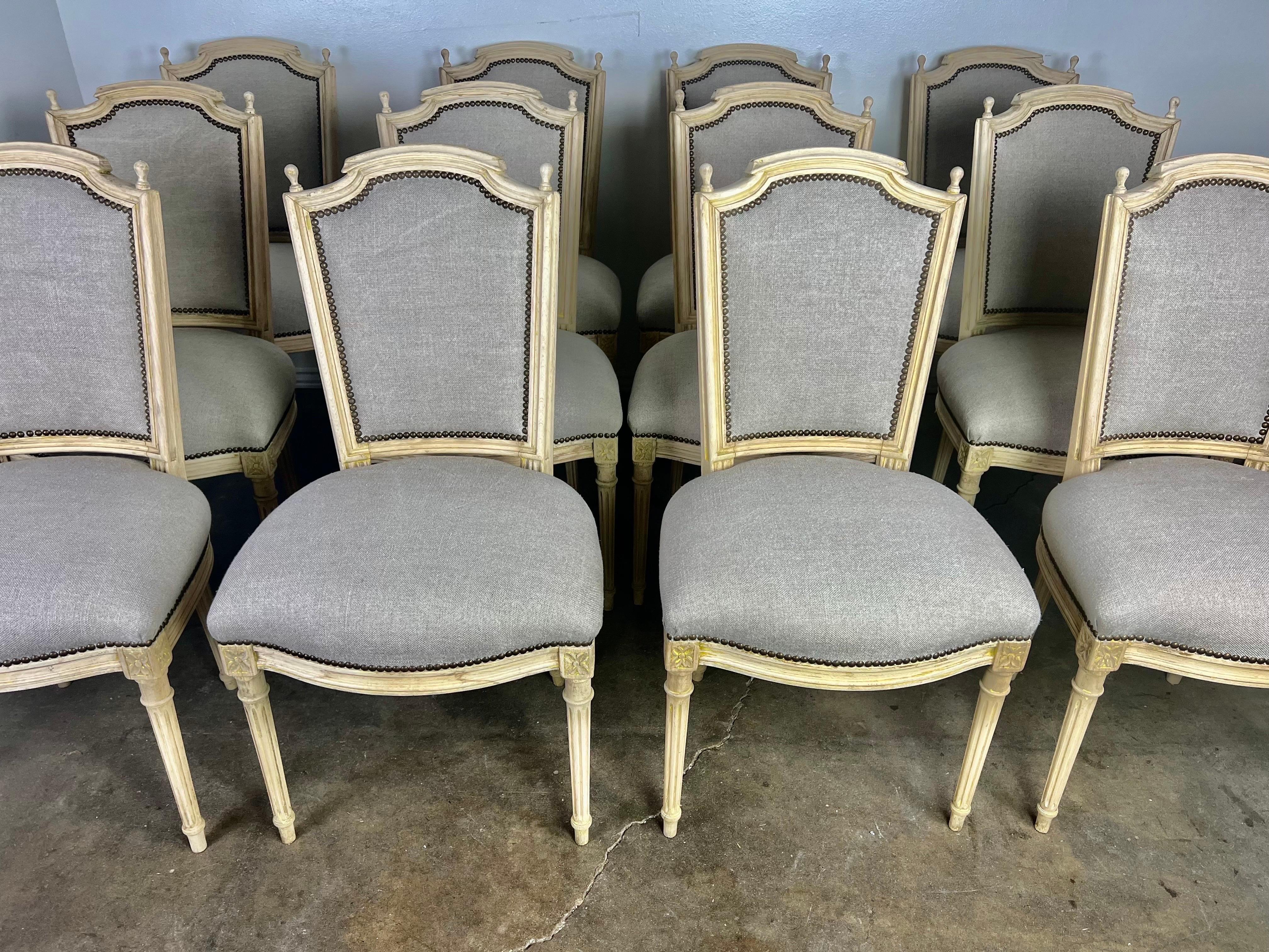 Set of (12) French Louis XVI style dining chairs. The chairs each stand on four straight fluted legs. The finish was originally paint, but the paint has been removed leaving a lovely natural finish behind. The chairs are newly reupholstered in a