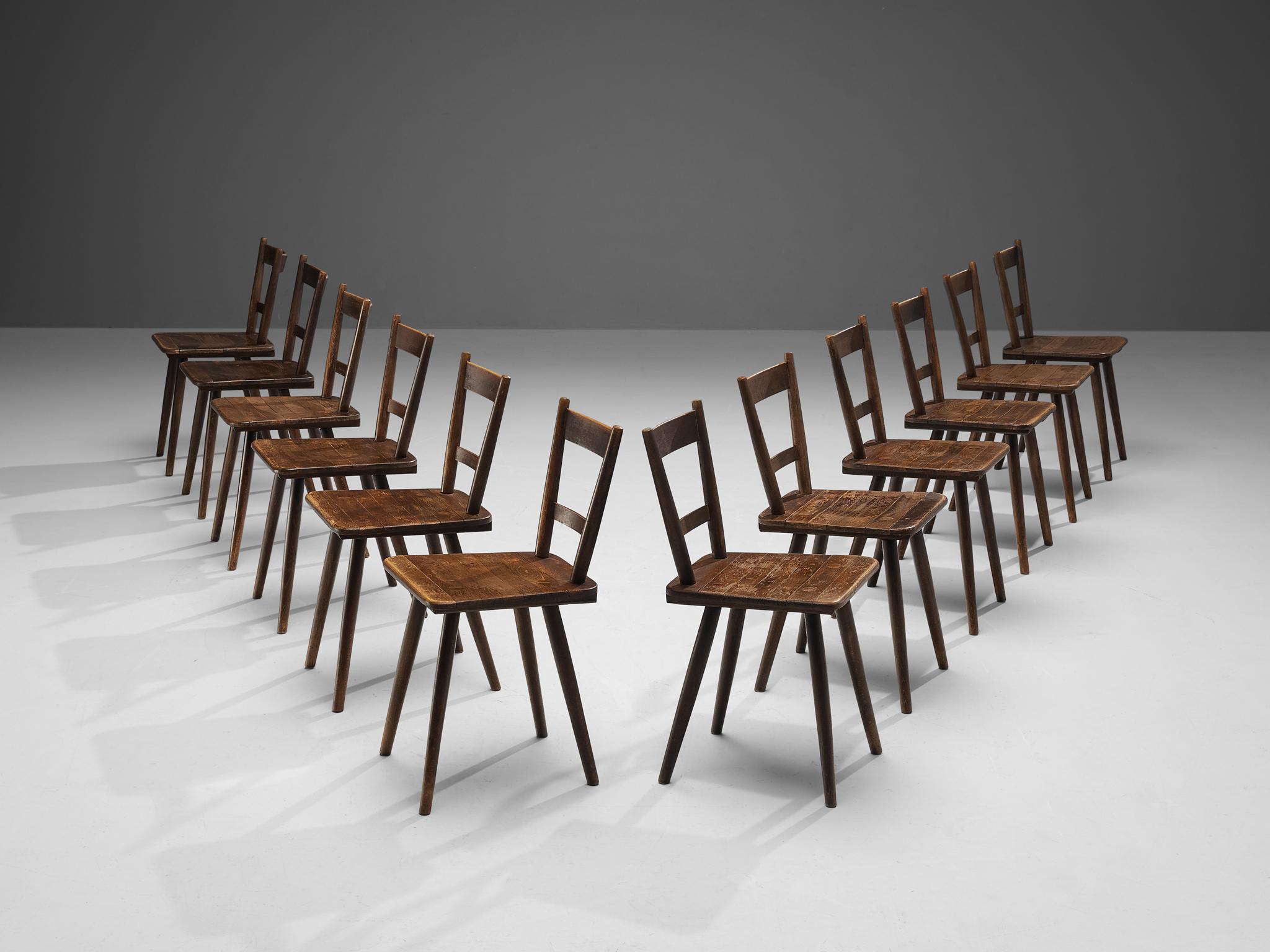 Set of twelve dining chairs, stained wood, France, late 1940s. 

Set of rustic dining chairs manufactured in France. Simple yet stylish, these chairs feature a modest frame with sleek, elegant elements. Note for example the tapered legs slightly