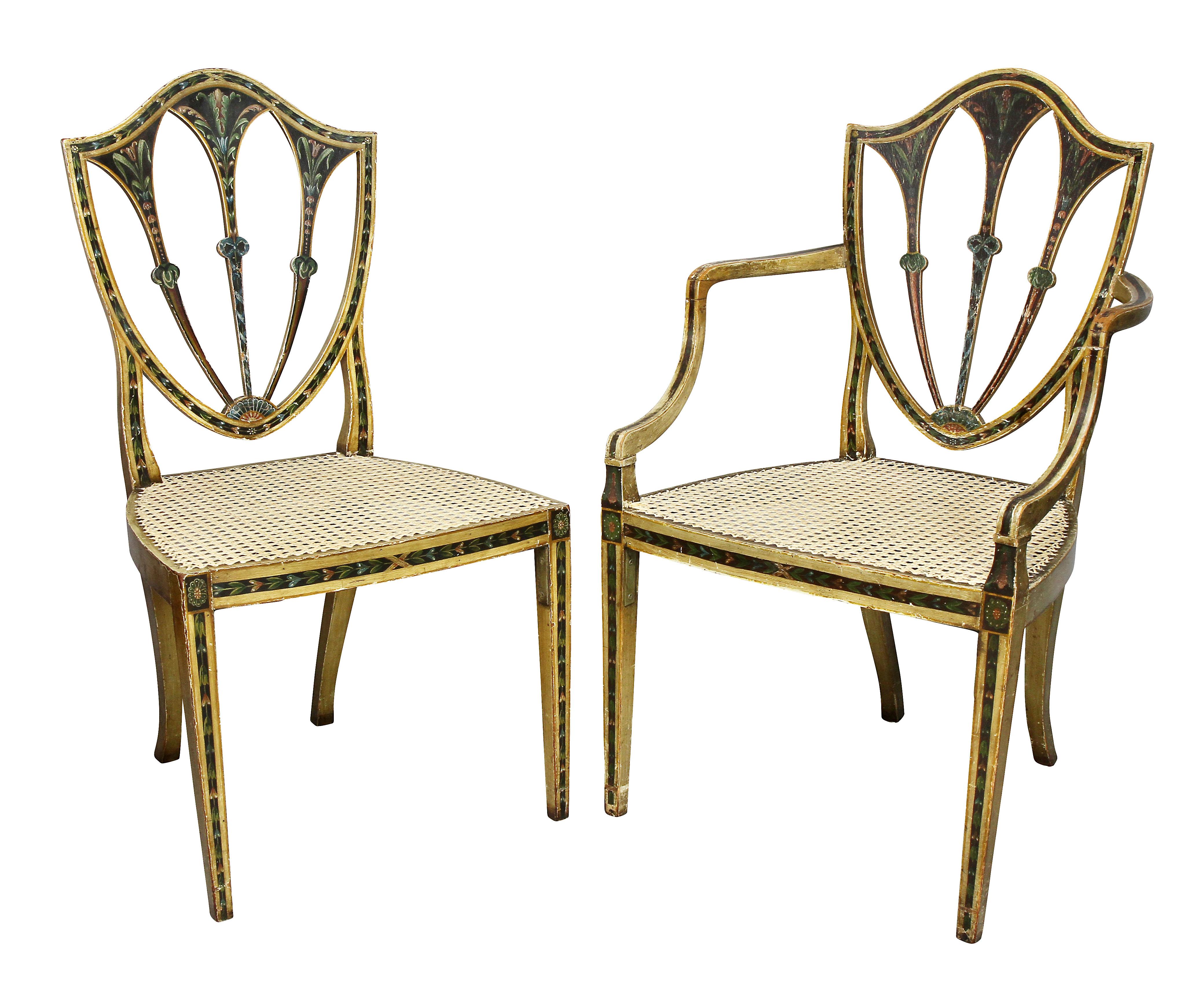 Comprising a pair of armchairs and 10 side chairs, each with a shield back and caned seats {all newly hand caned] raised on square tapered legs. Paint decoration in a variety of condition some worn more than others. They have a country more rustic