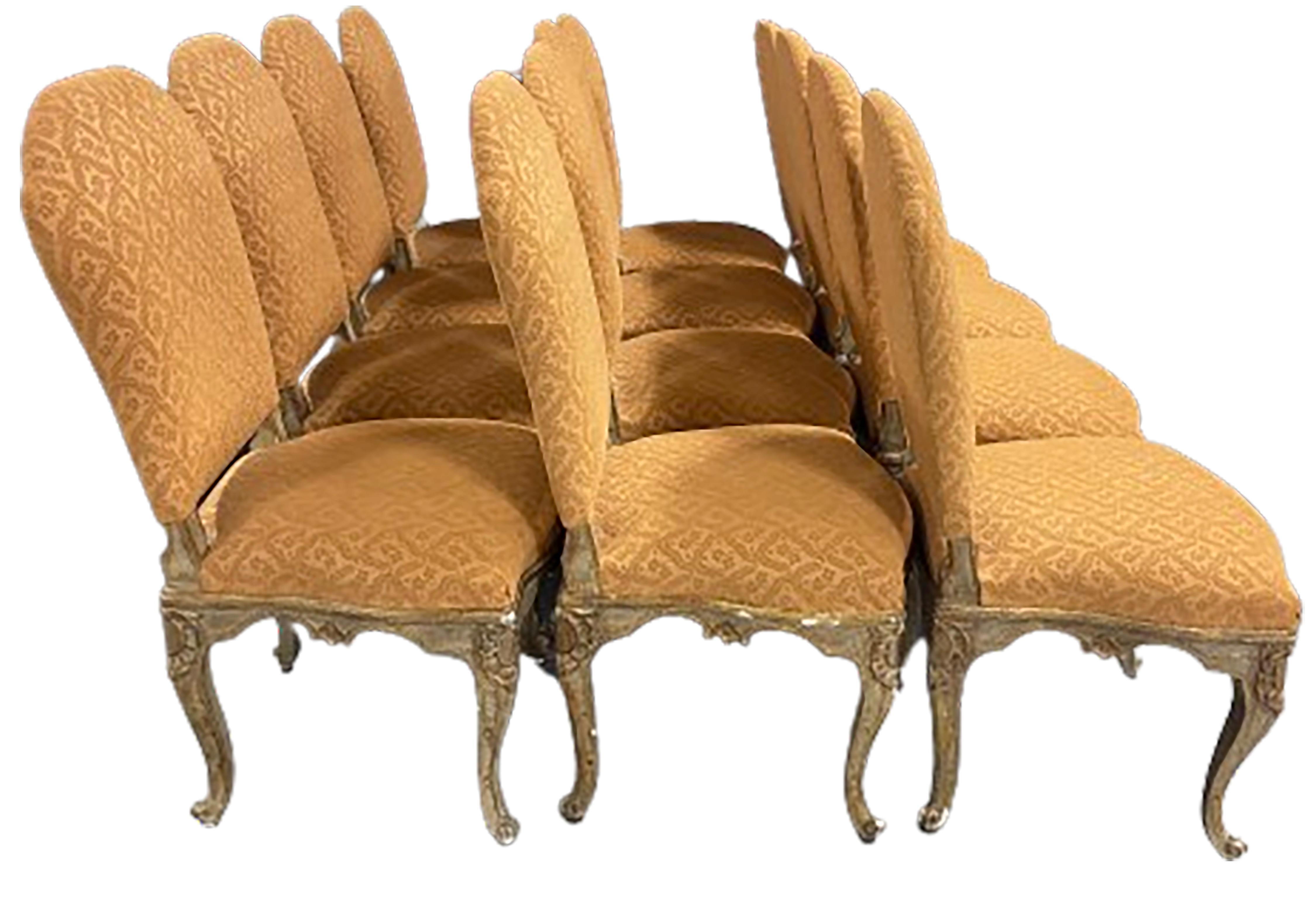 Ein eleganter Satz von zwölf Esszimmerstühlen im Stil Louis XV. Senfgoldfarbener, gepolsterter Stoff mit Cabriole-Holzbeinen. Leicht abgewinkelte Rückenlehnen und ein  dunkler, vergoldeter Sockel. 

In gutem Zustand. Alters- und gebrauchsbedingte