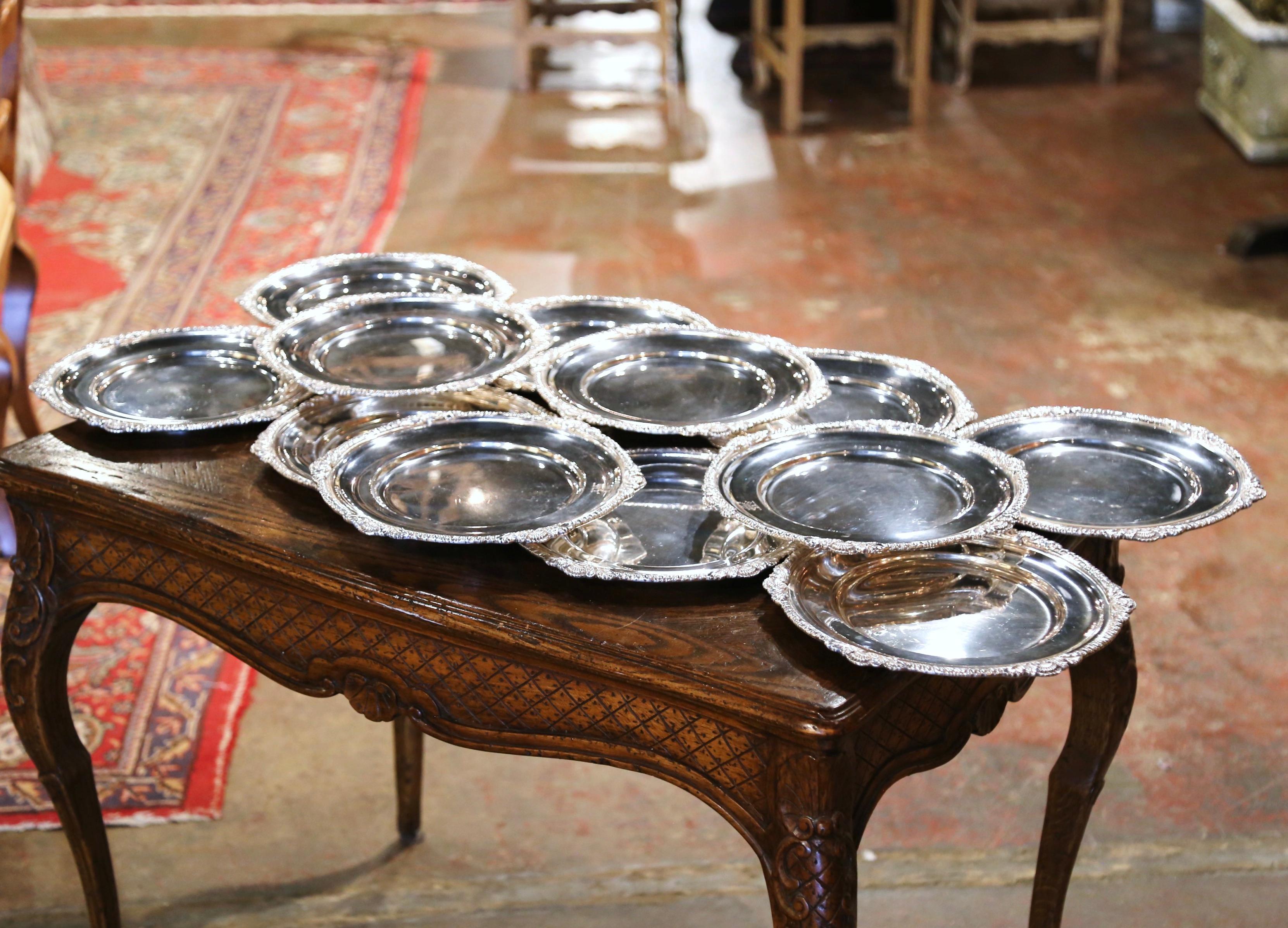 Dress your dining table with elegance using this midcentury set under plate. Crafted in France circa 1950, each silverplated charger features ornate scroll and shell decor throughout the rim of the plate. Displayed on each service plate is a group